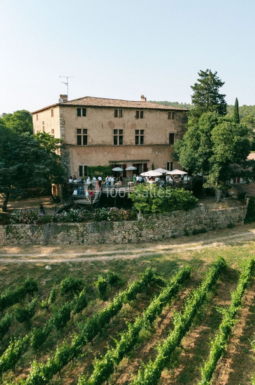 Vue aérienne d'un domaine avec un bâtiment en pierre, une terrasse animée et des vignes au premier plan.
