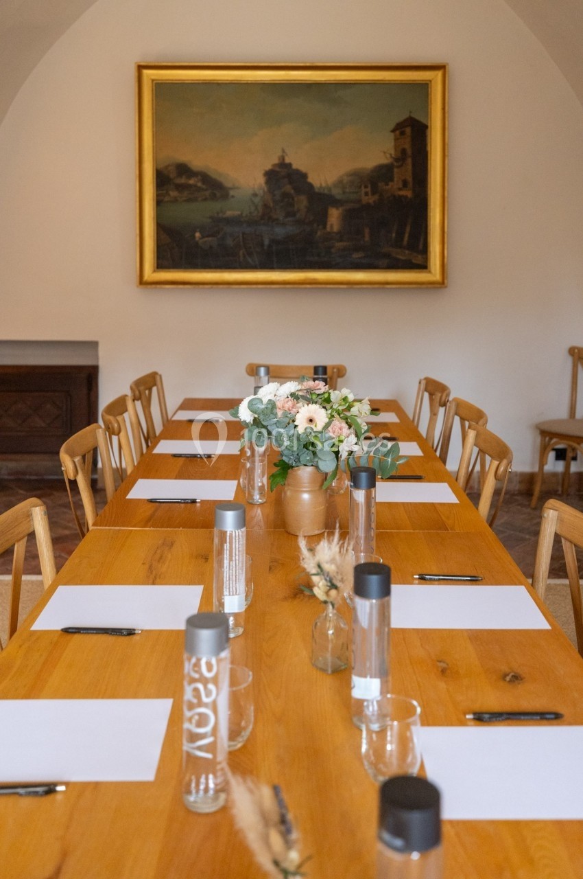 Salle de réunion avec une grande table en bois, des chaises assorties et un bouquet de fleurs au centre.