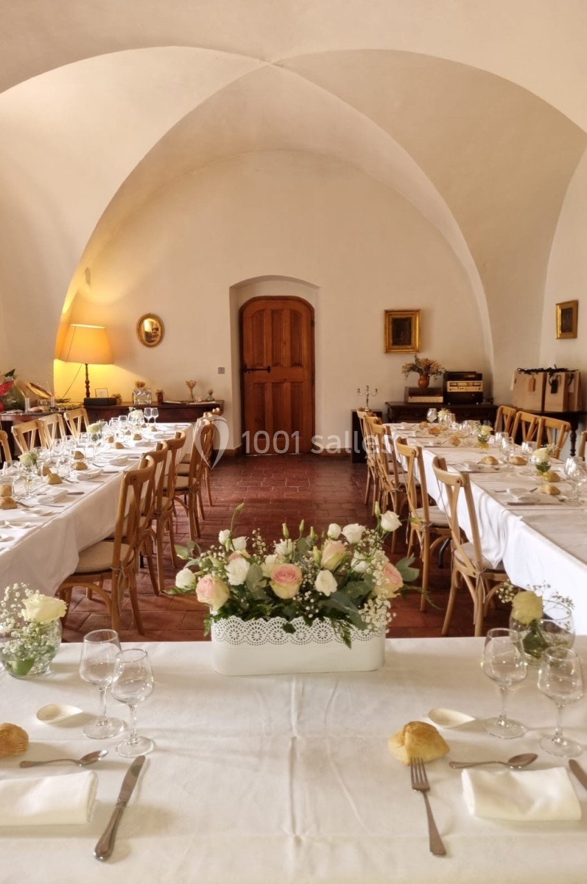 Salle de réception élégante avec tables dressées, nappes blanches, vaisselle et centre de table floral.