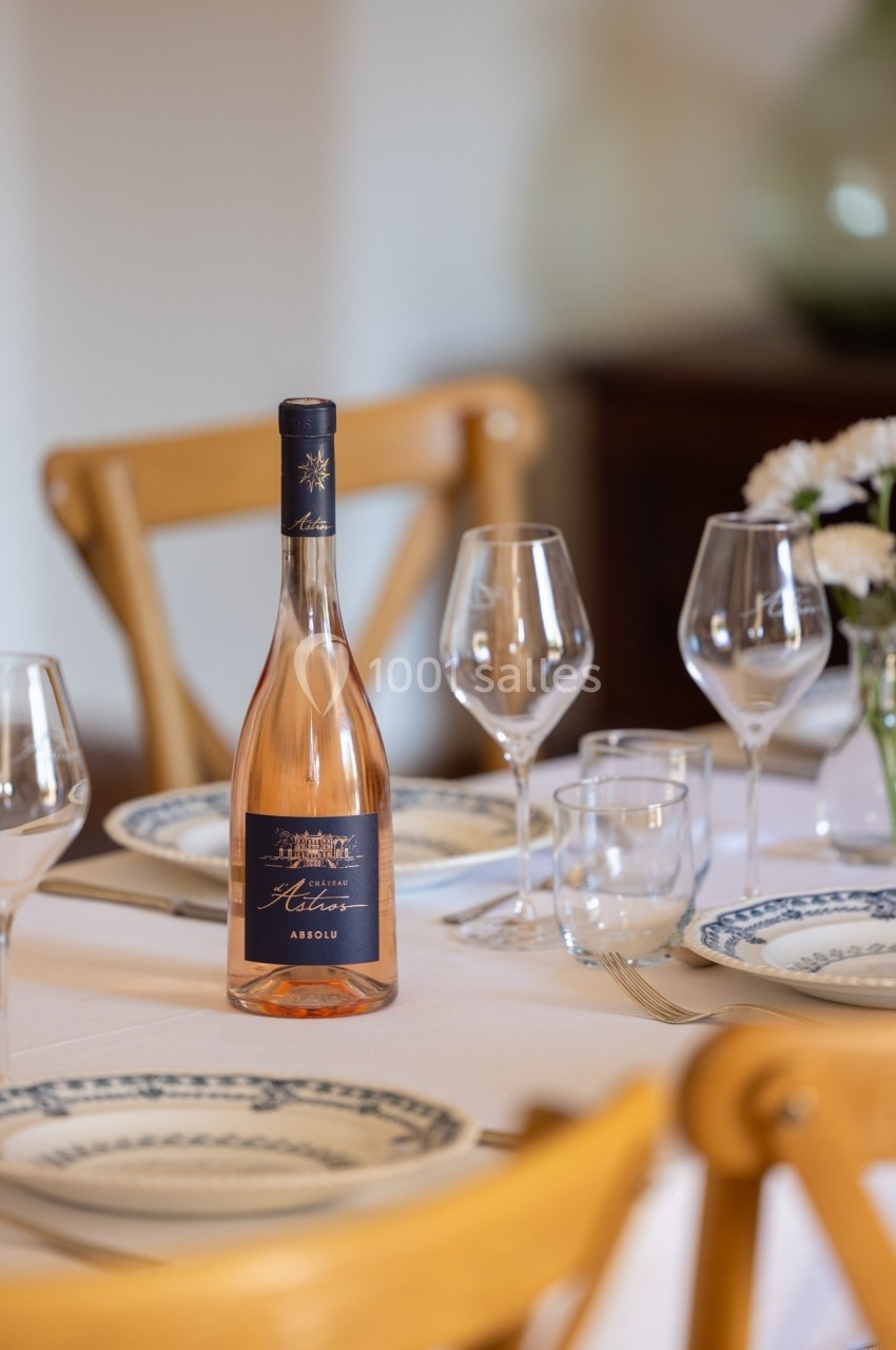 Bouteille de vin rosé posée sur une table dressée avec assiettes, verres et fleurs en arrière-plan.