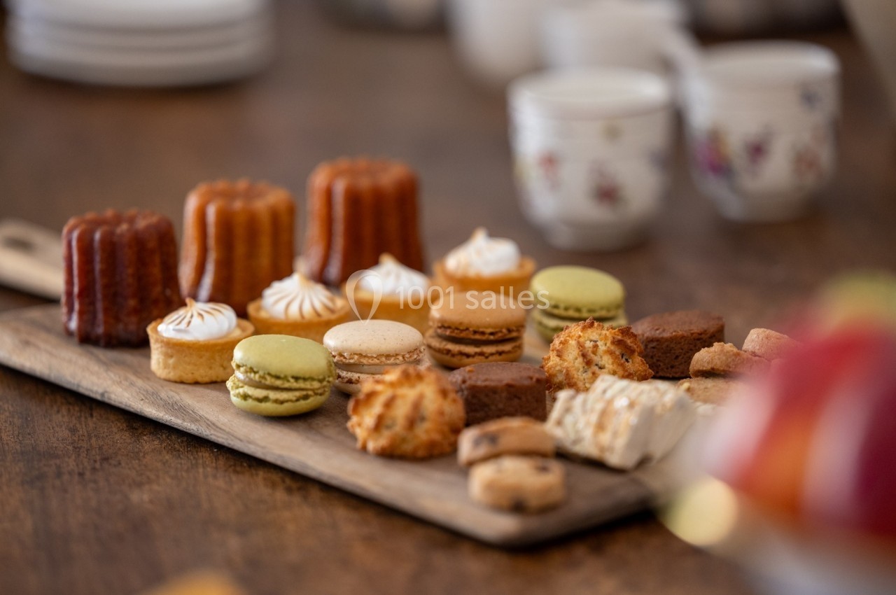 Plateau en bois avec un assortiment de pâtisseries françaises, macarons, cannelés et autres douceurs, sur une table en bois.