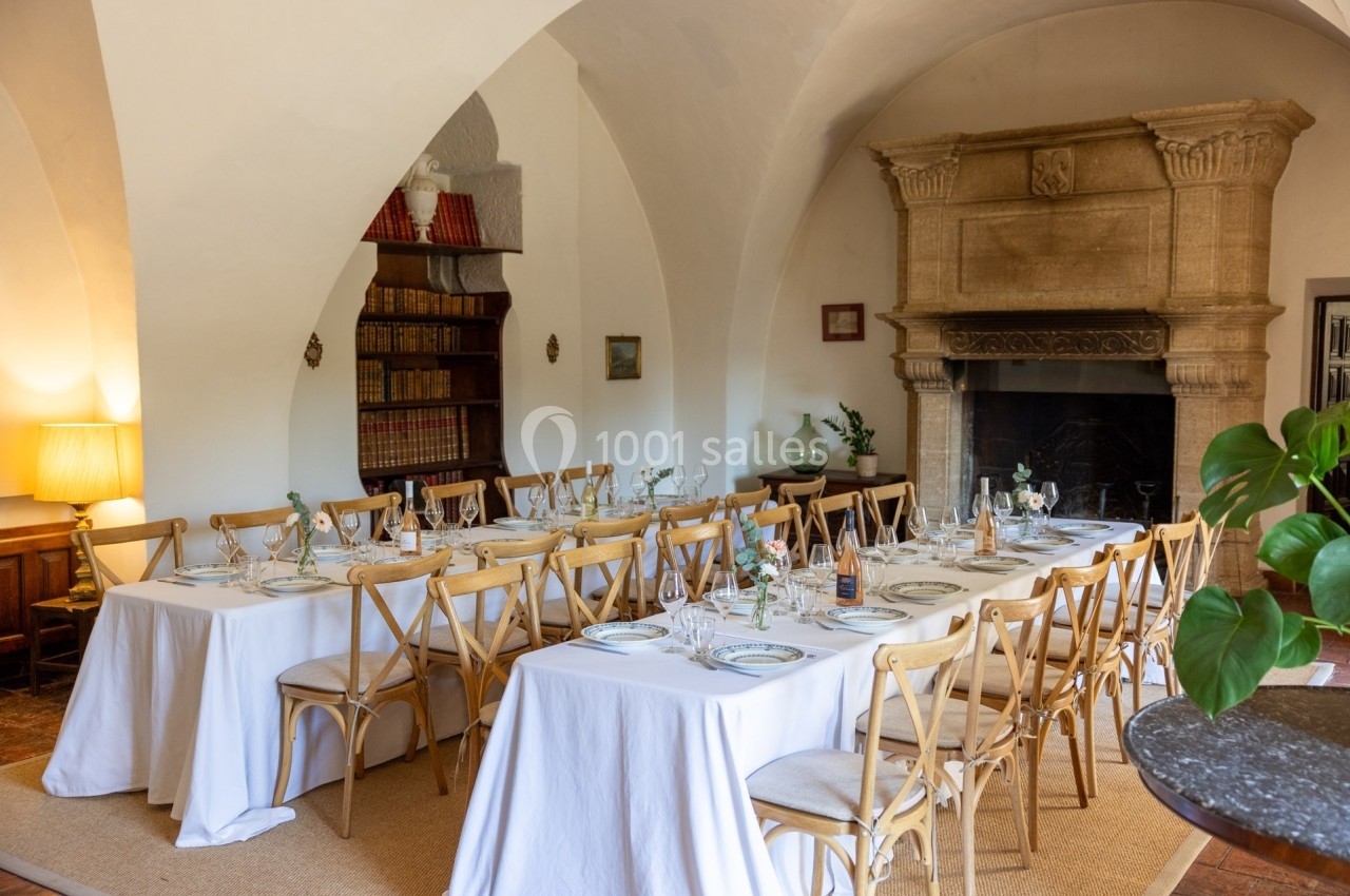 Salle à manger élégante avec tables dressées, chaises en bois, cheminée en pierre et étagères remplies de livres.