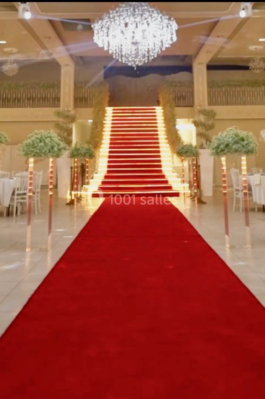 Escalier illuminé avec tapis rouge, entouré de tables blanches et de décorations florales dans une salle de réception…
