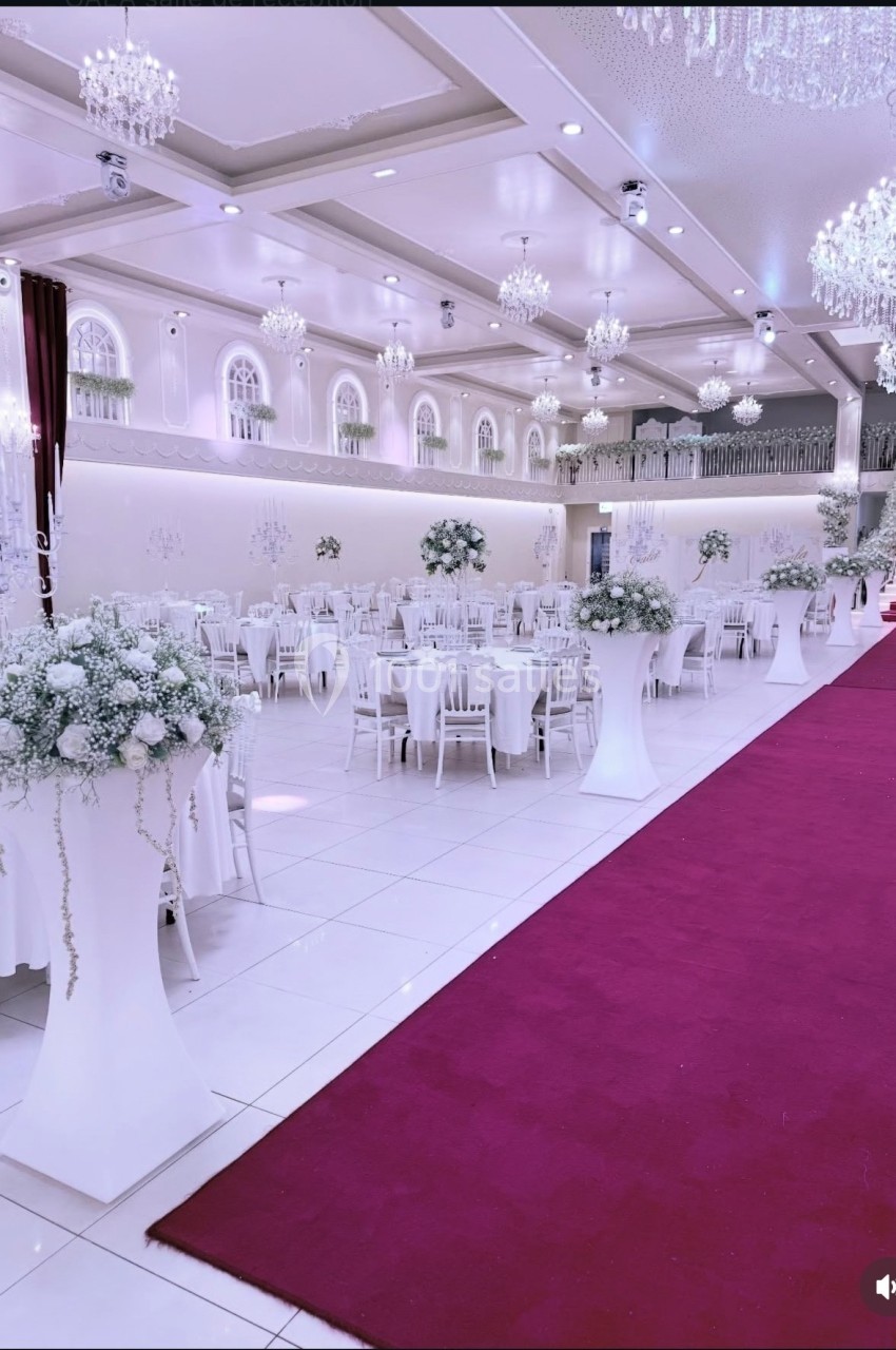 Salle de réception élégante avec tables décorées, chandeliers suspendus et tapis rouge menant à un escalier.