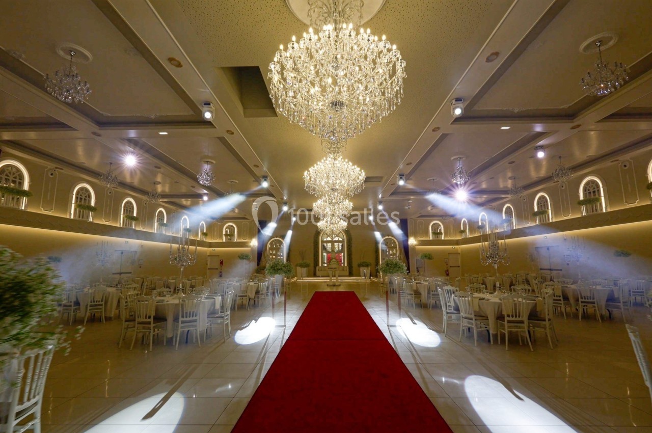 Salle de réception élégante avec lustres en cristal, tables dressées et tapis rouge au centre.