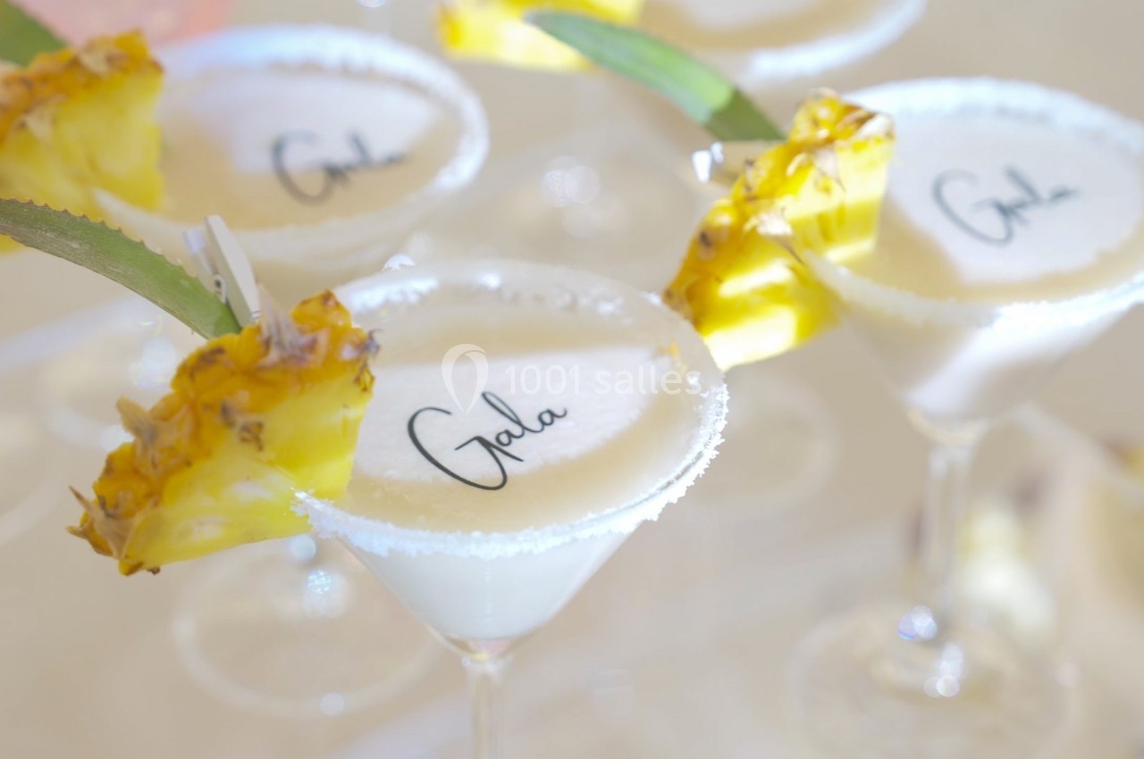 Verres à cocktail garnis de tranches d'ananas et de sucre sur le bord, avec ’Gala’ inscrit sur la mousse.