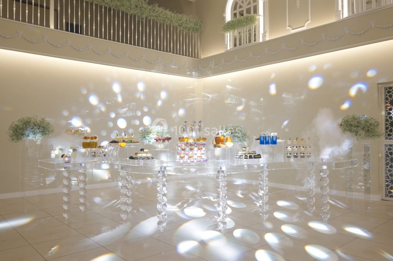 Table transparente décorée avec des desserts variés, entourée de bouquets de gypsophiles dans une salle lumineuse.
