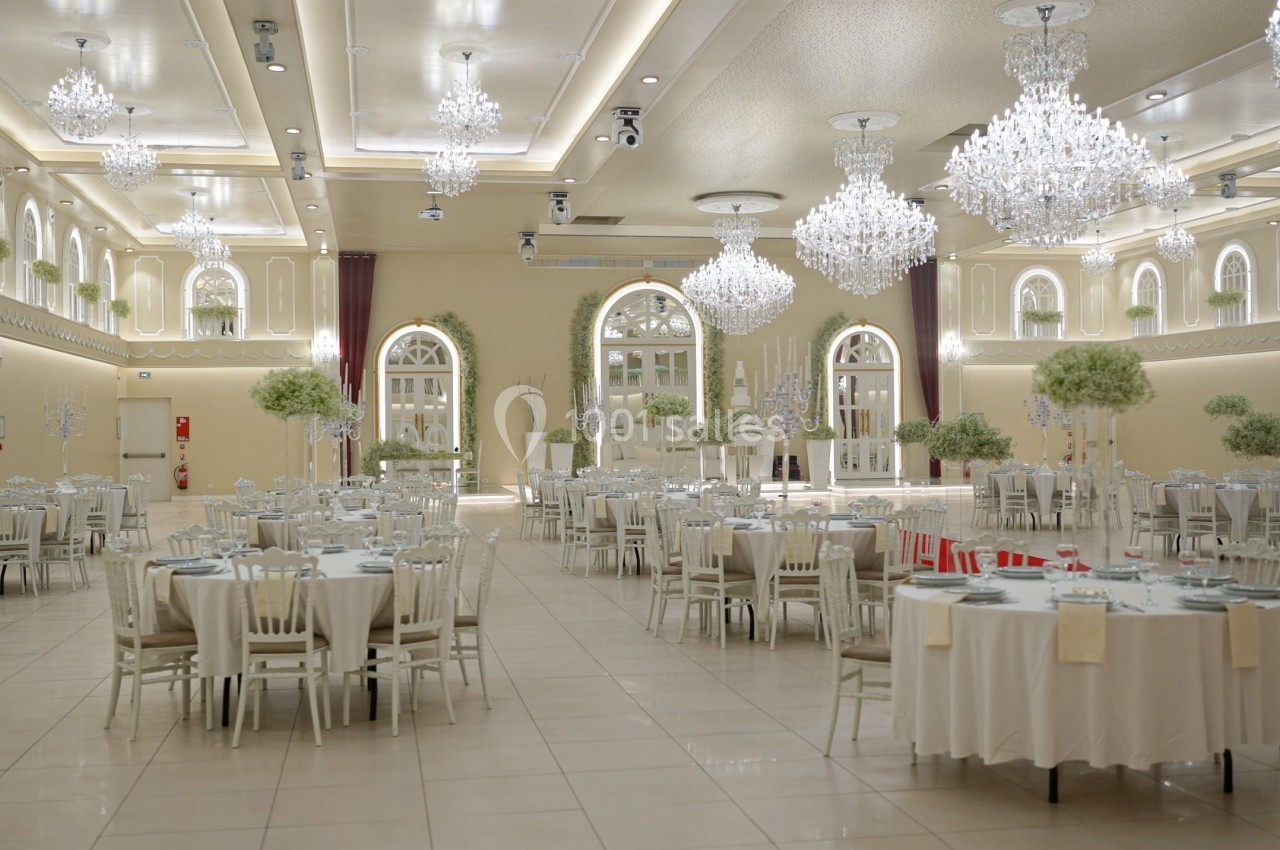 Salle de réception élégante avec tables dressées, lustres scintillants et décorations florales blanches.
