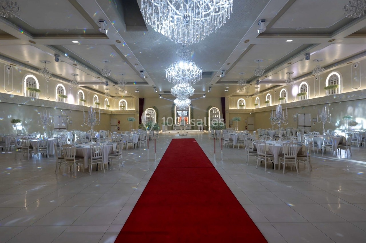 Salle de réception élégante avec tables dressées, lustres imposants et tapis rouge central.