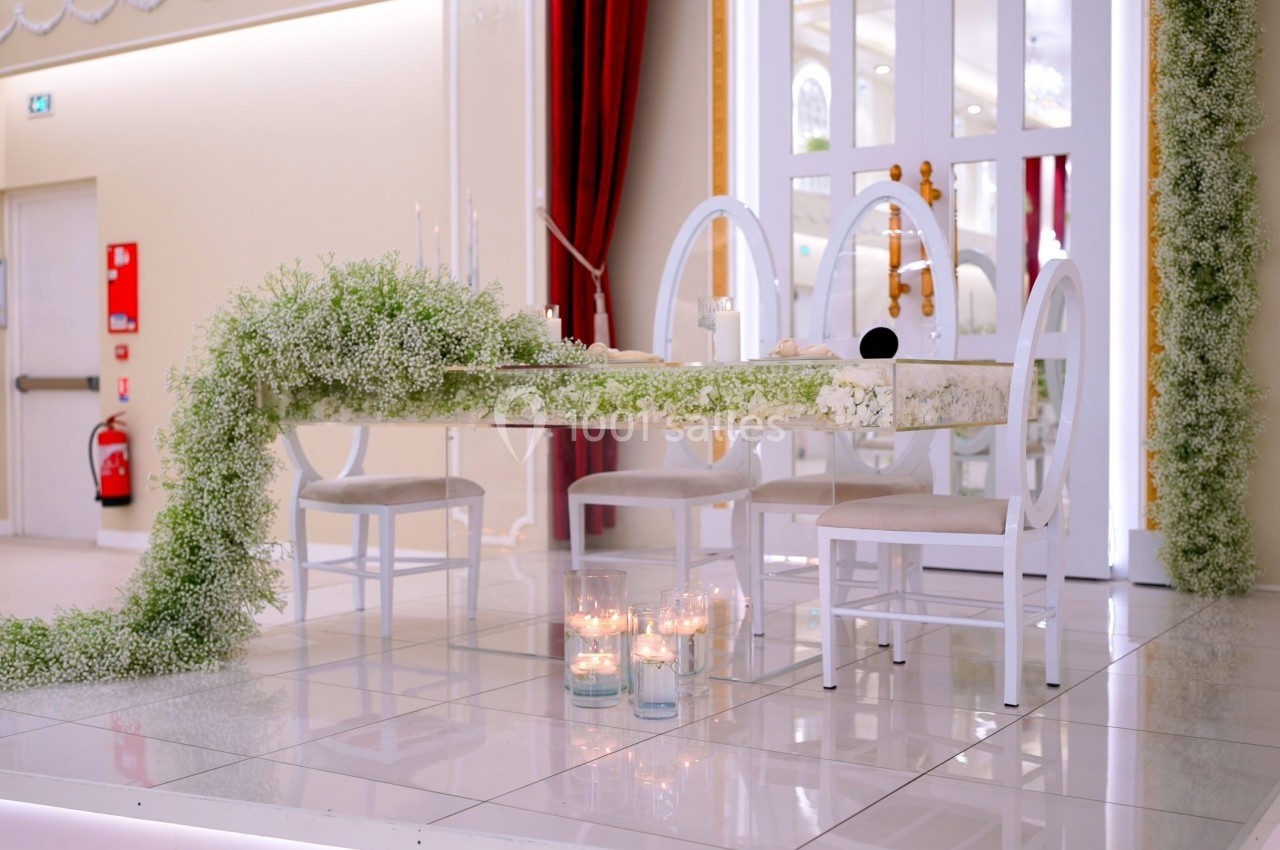 Table décorée de fleurs blanches avec des chaises assorties, entourée de bougies et située dans une salle lumineuse.