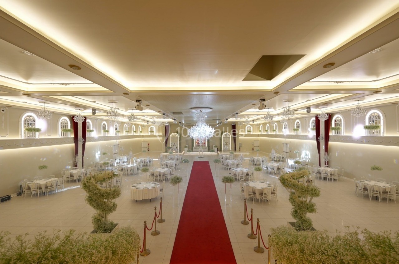Salle de réception élégante avec tables dressées, tapis rouge central et éclairage lumineux.