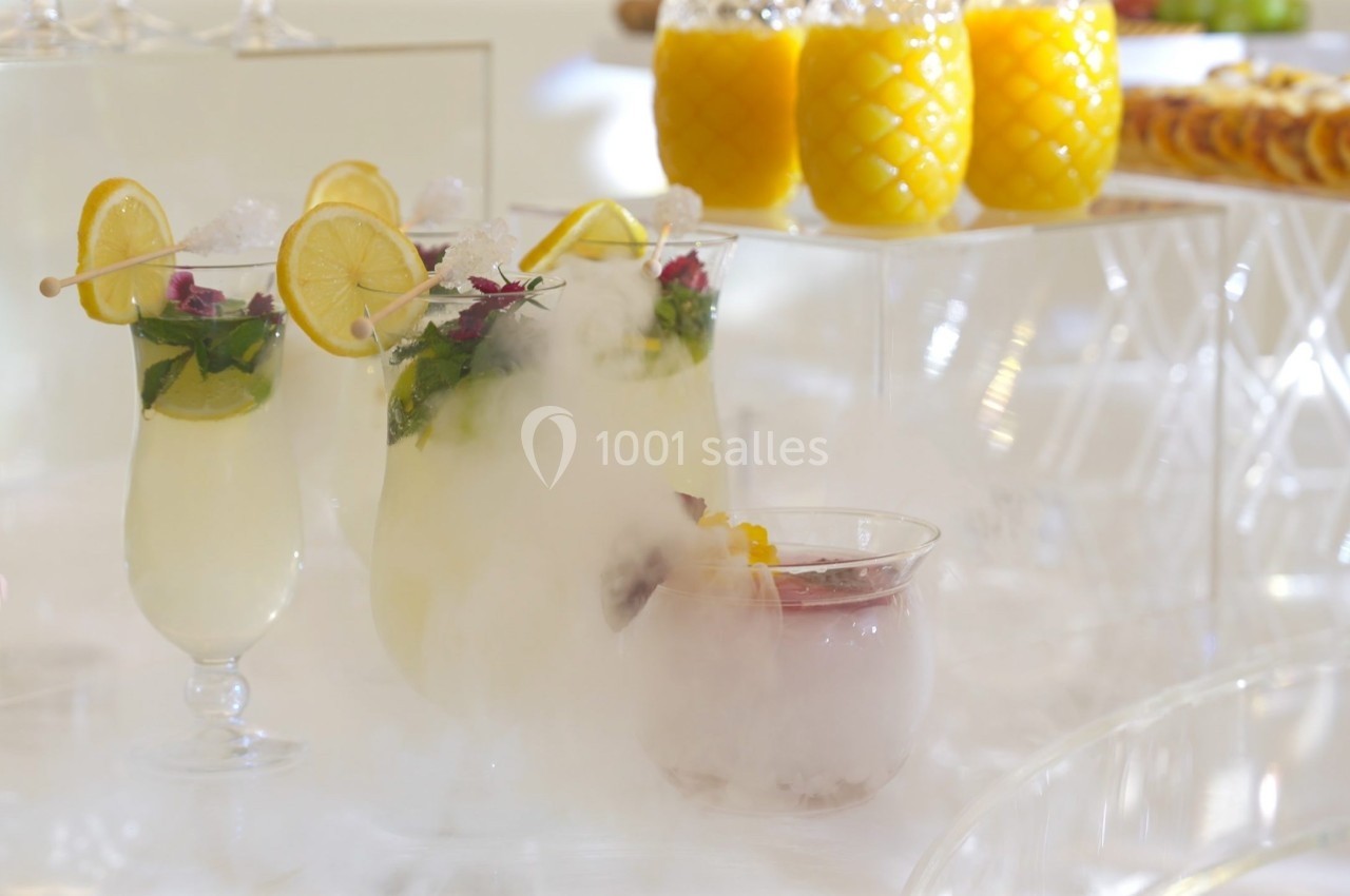 Verres de cocktails décorés de tranches de citron et de menthe, entourés de vapeur blanche sur une table lumineuse.