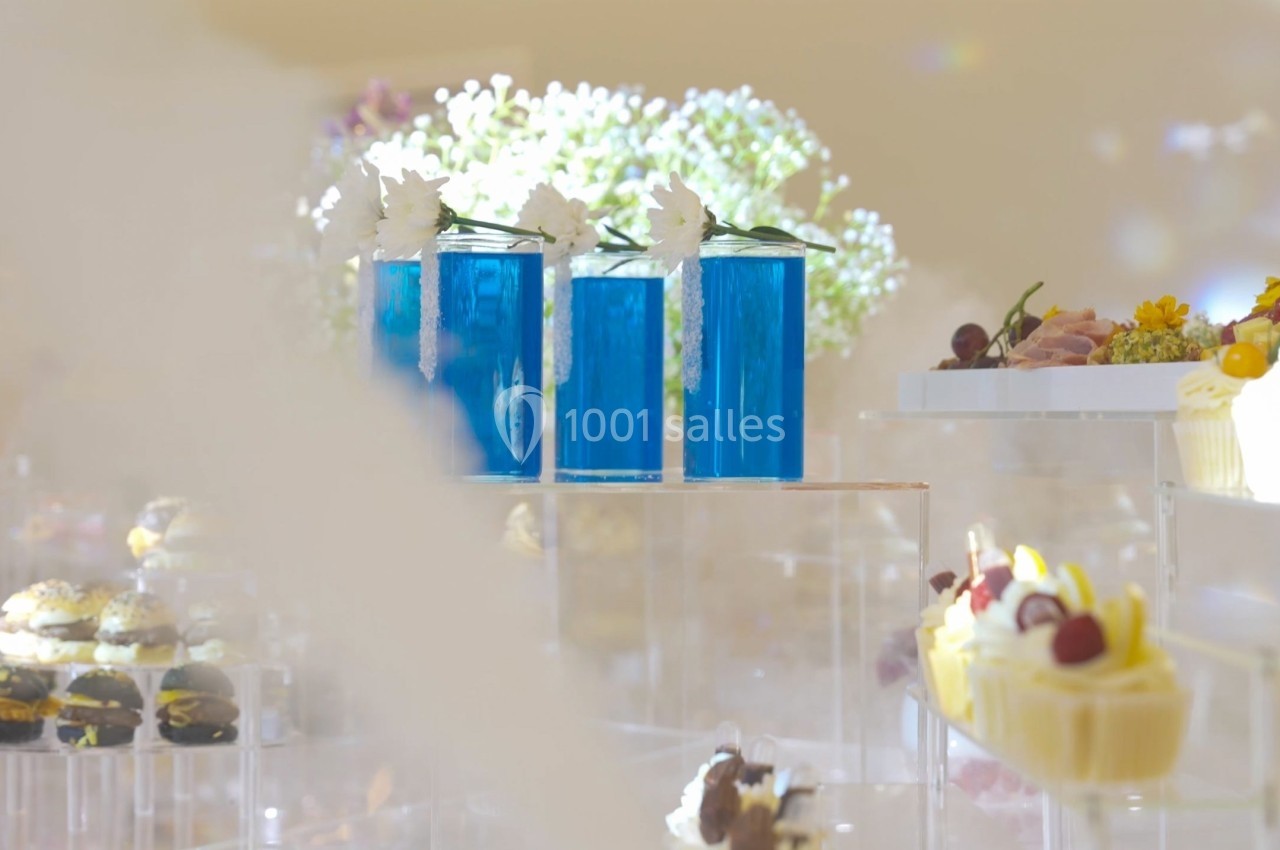 Présentoirs transparents avec desserts variés et trois verres de cocktail bleus décorés de fleurs blanches.