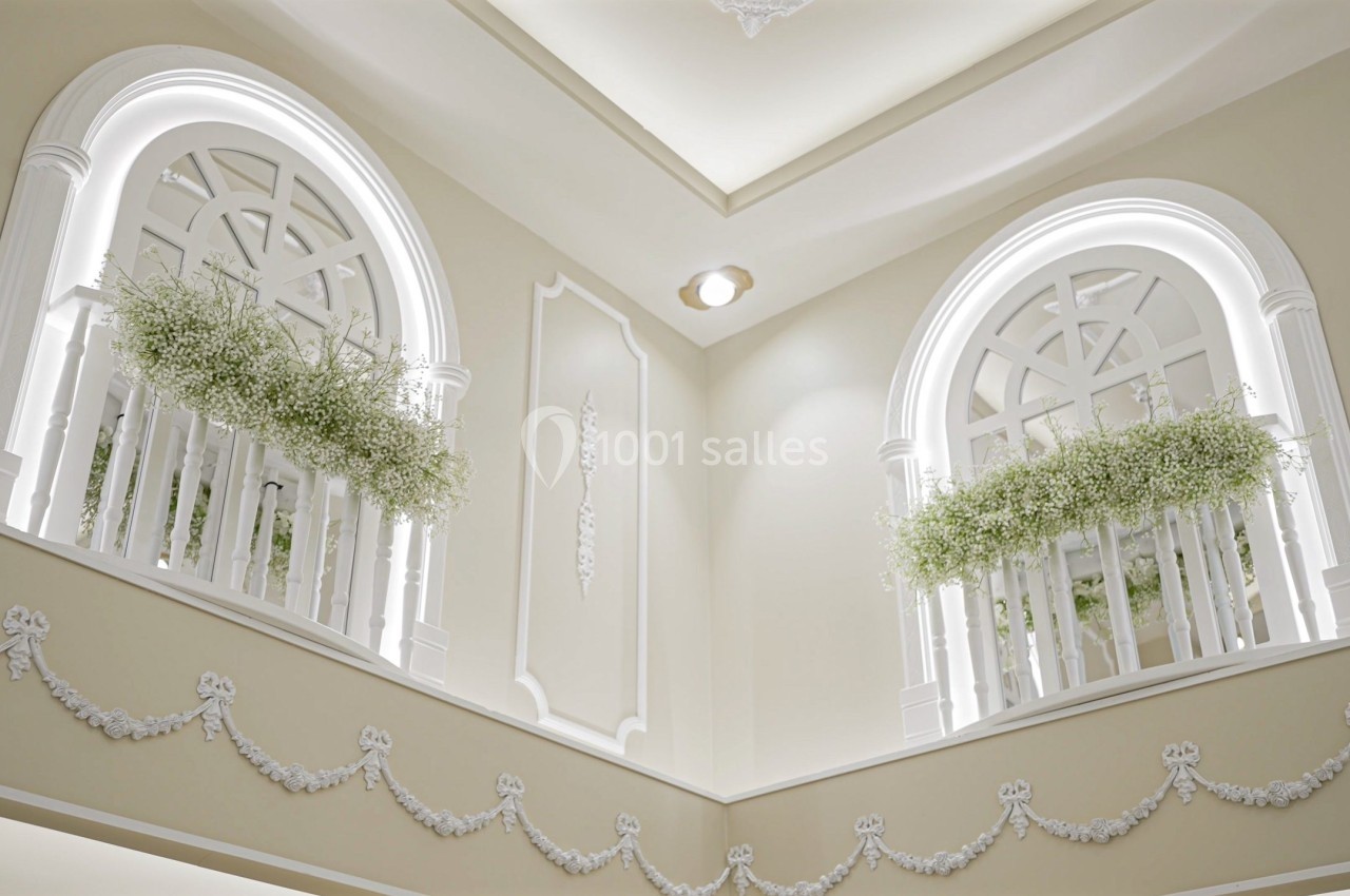 Deux fenêtres cintrées décorées de balustrades blanches et de plantes vertes dans un intérieur lumineux et élégant.