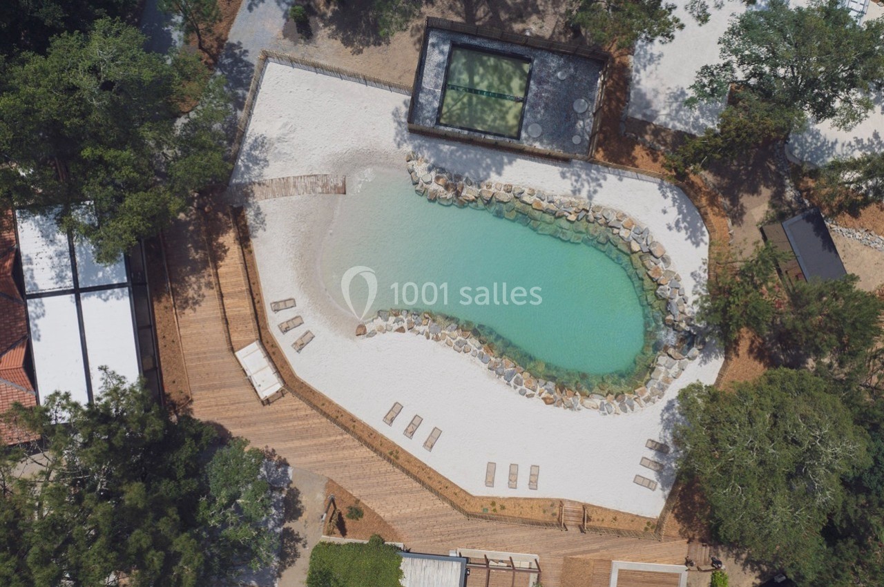 Vue aérienne d'une piscine naturelle entourée de sable, de chaises longues et de végétation.