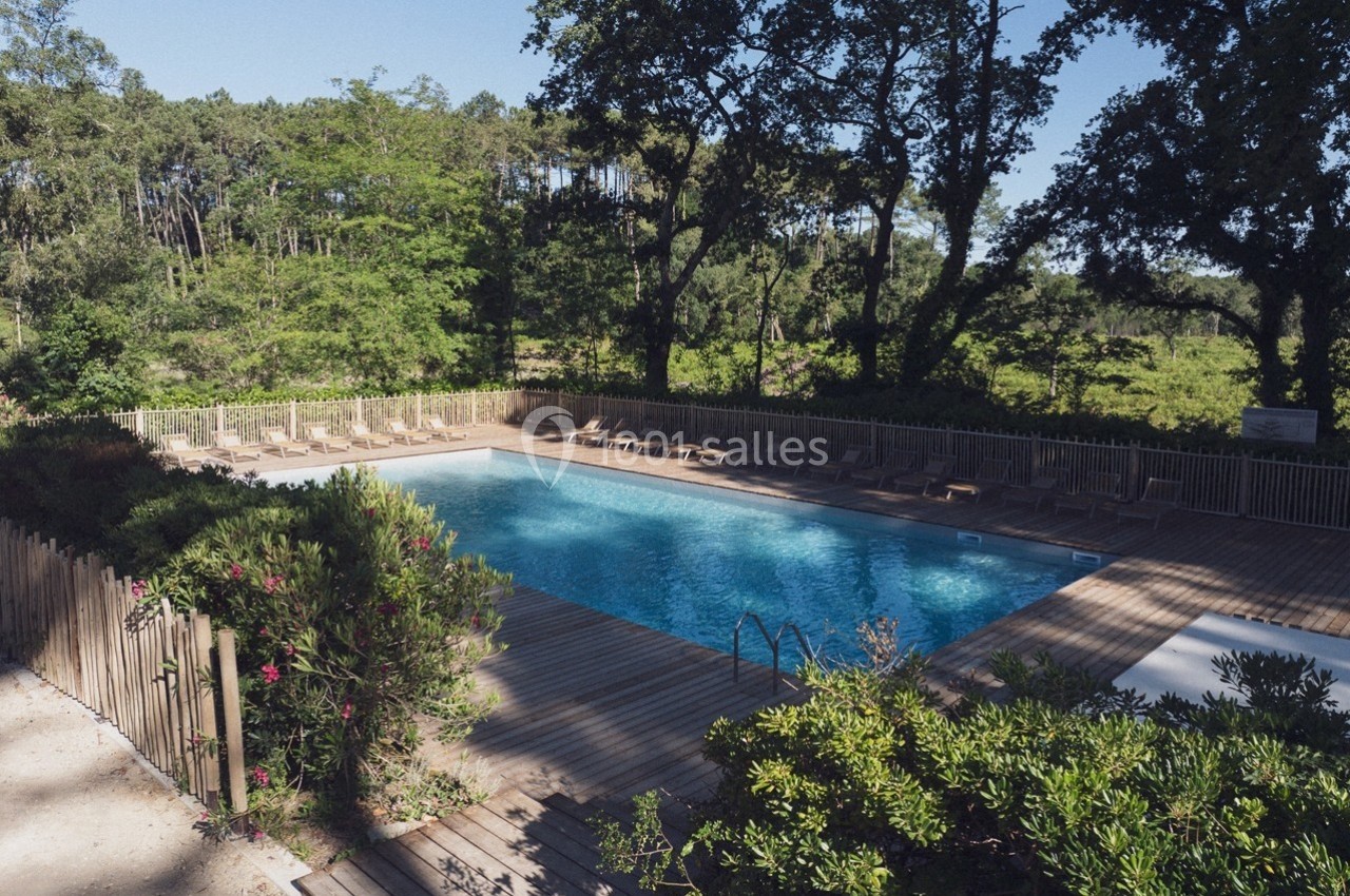 Piscine extérieure entourée de végétation, avec des transats disposés sur une terrasse en bois.