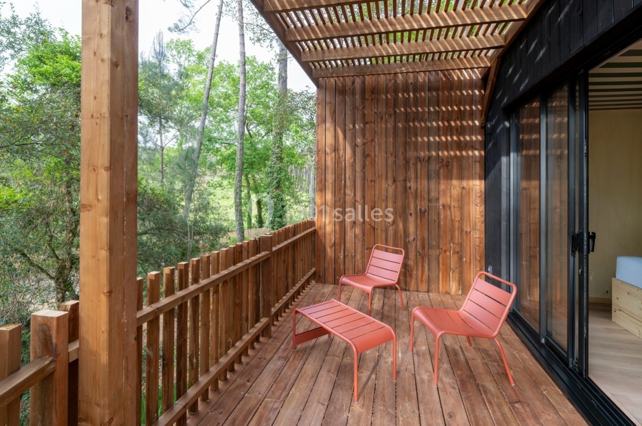 Terrasse en bois avec trois chaises rouges, entourée de verdure et partiellement ombragée par une pergola.