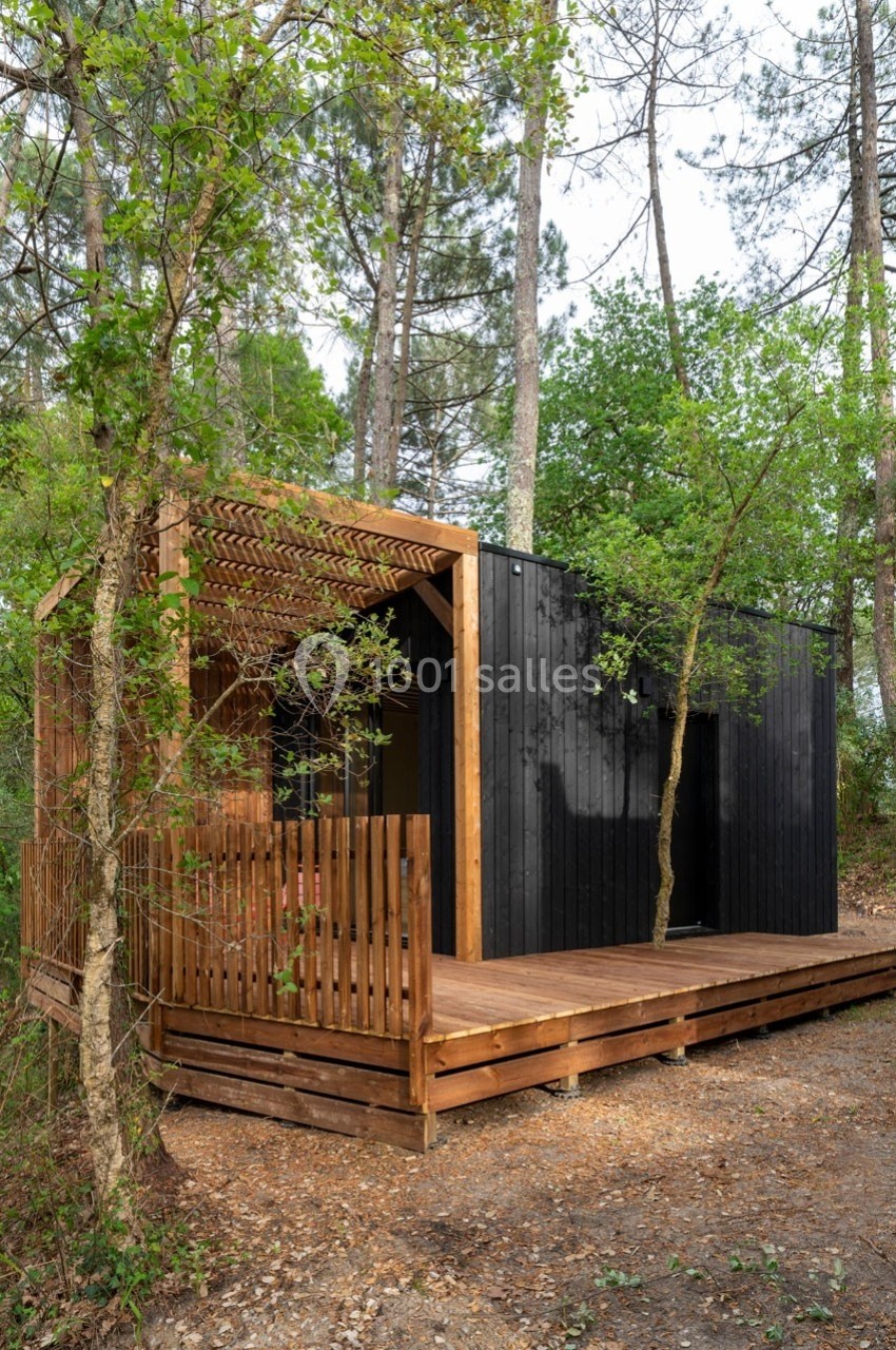 Cabane moderne en bois noir et naturel avec terrasse, entourée de pins et de végétation dense.