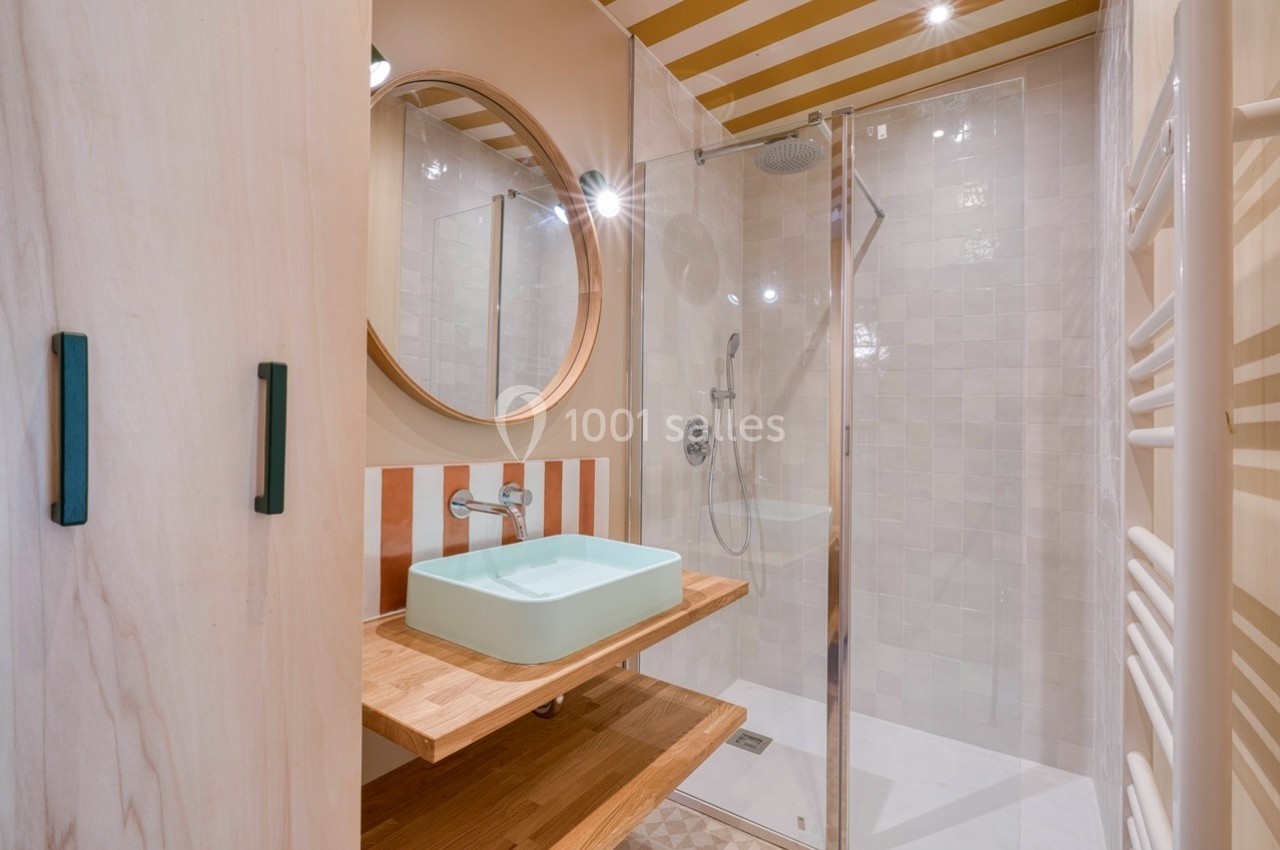 Salle de bain avec douche à l'italienne, lavabo sur planche en bois, miroir rond et murs aux tons clairs.