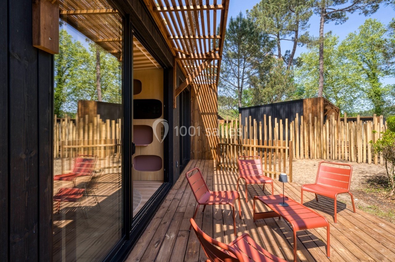Terrasse en bois avec mobilier rouge, entourée de palissades en bois et de végétation sous un ciel dégagé.