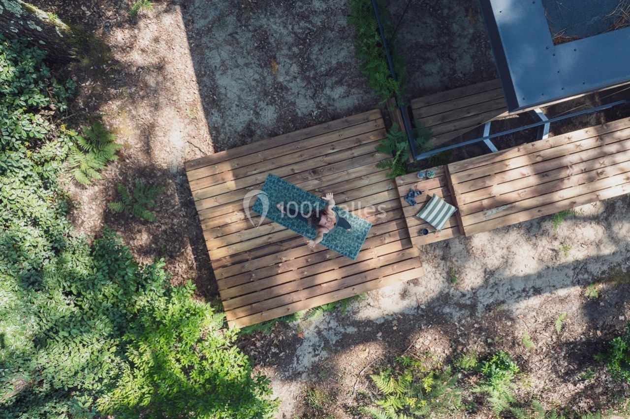 Vue aérienne d'une personne assise sur une terrasse en bois entourée de végétation.