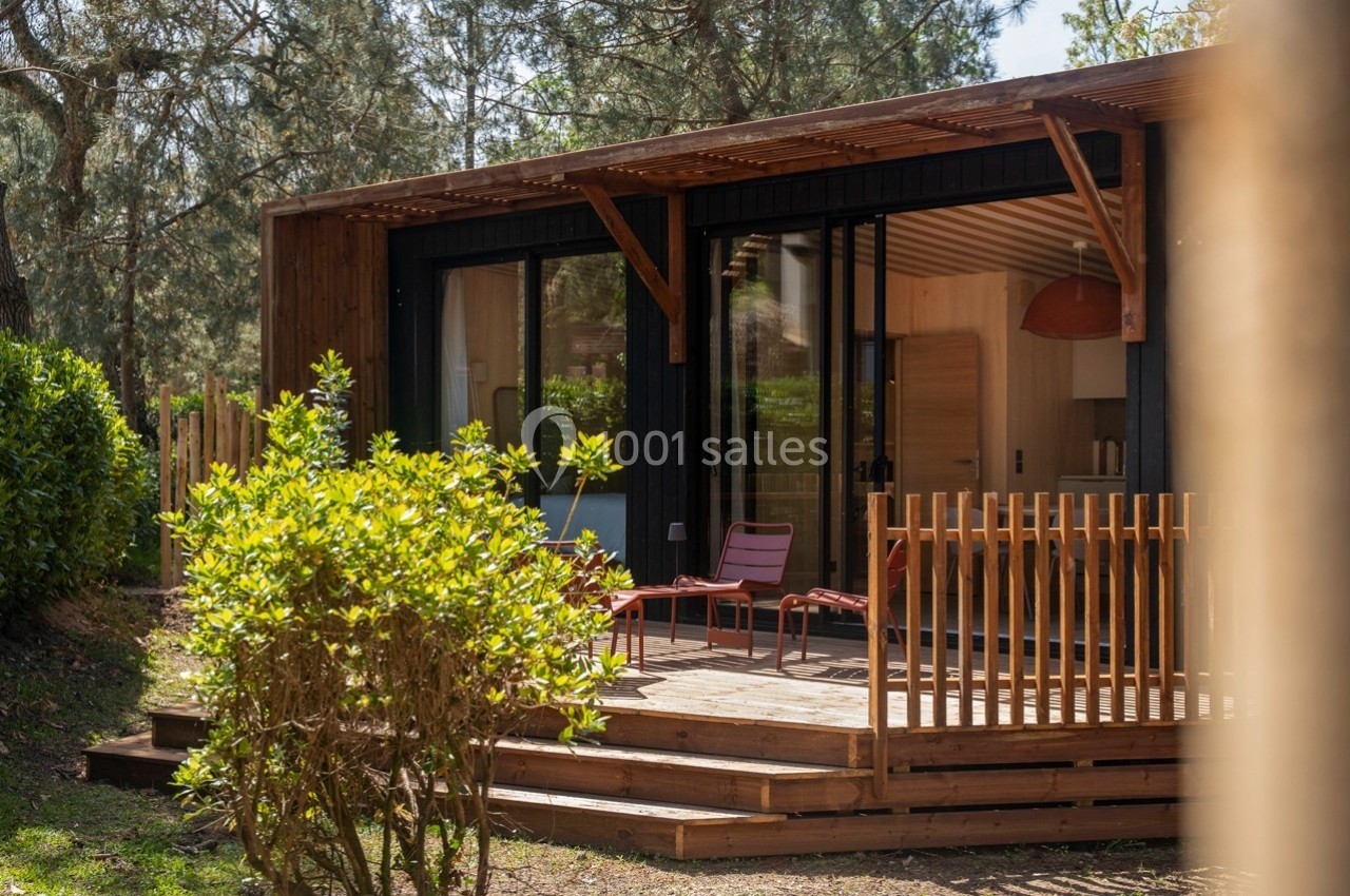 Terrasse en bois avec fauteuils devant une maison moderne entourée de végétation et de pins.