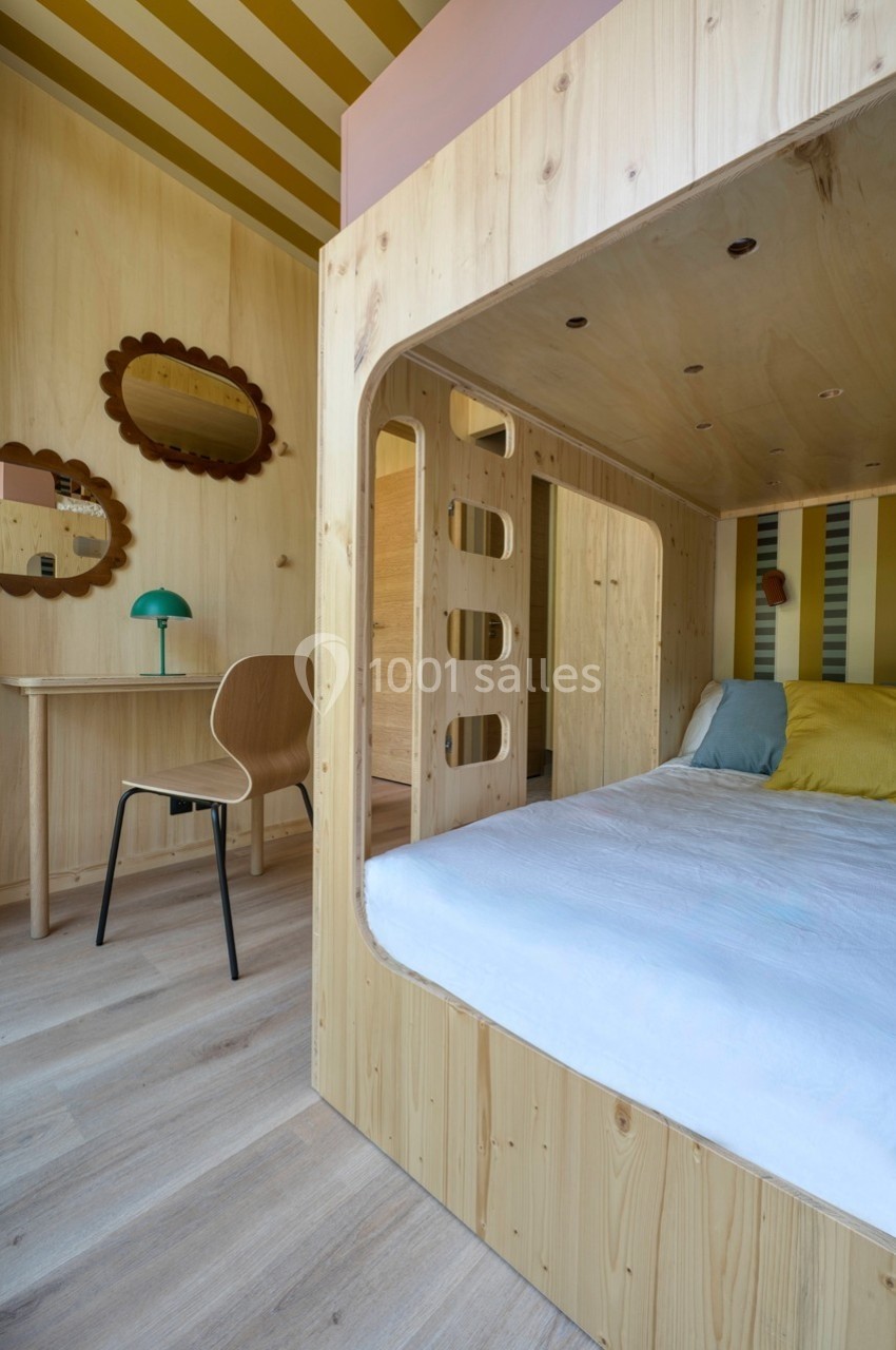 Lit superposé en bois clair avec bureau assorti, chaise et miroir mural dans une chambre lumineuse aux tons jaunes.