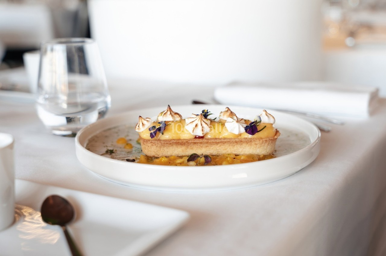 Tartelette garnie de crème citron, meringue et fleurs comestibles, servie sur une assiette blanche.