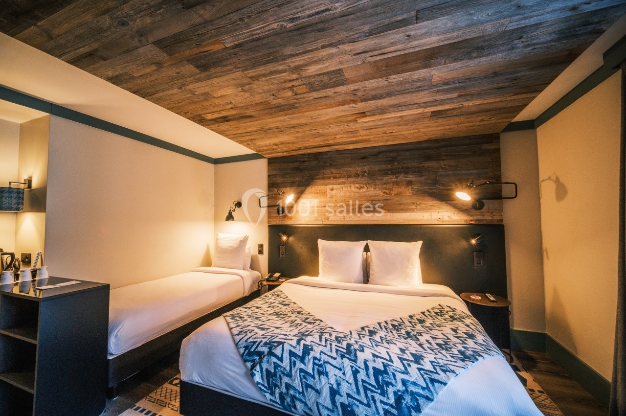 Chambre d'hôtel avec un lit double, un lit simple, un éclairage mural et un plafond en bois.