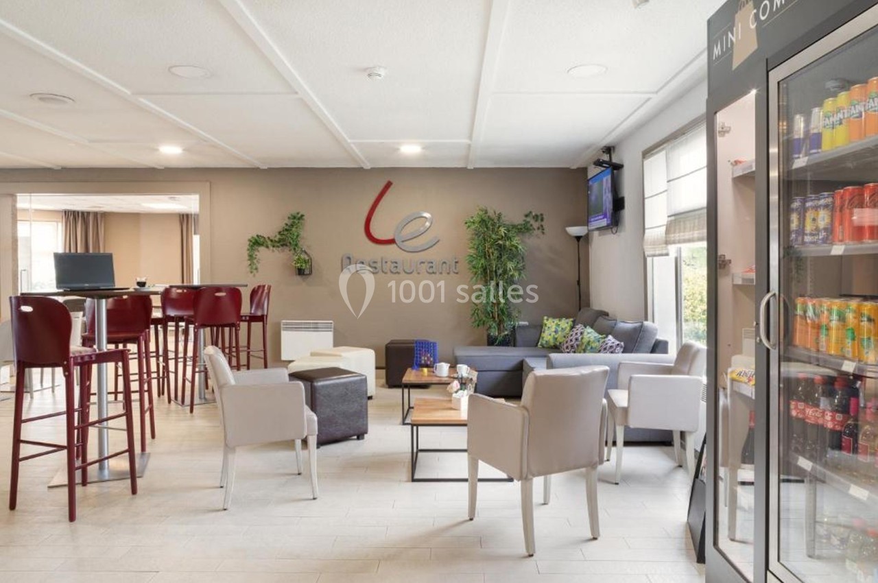 Espace lounge lumineux avec fauteuils, tables basses, distributeur de boissons et décoration végétale sur un mur beige.