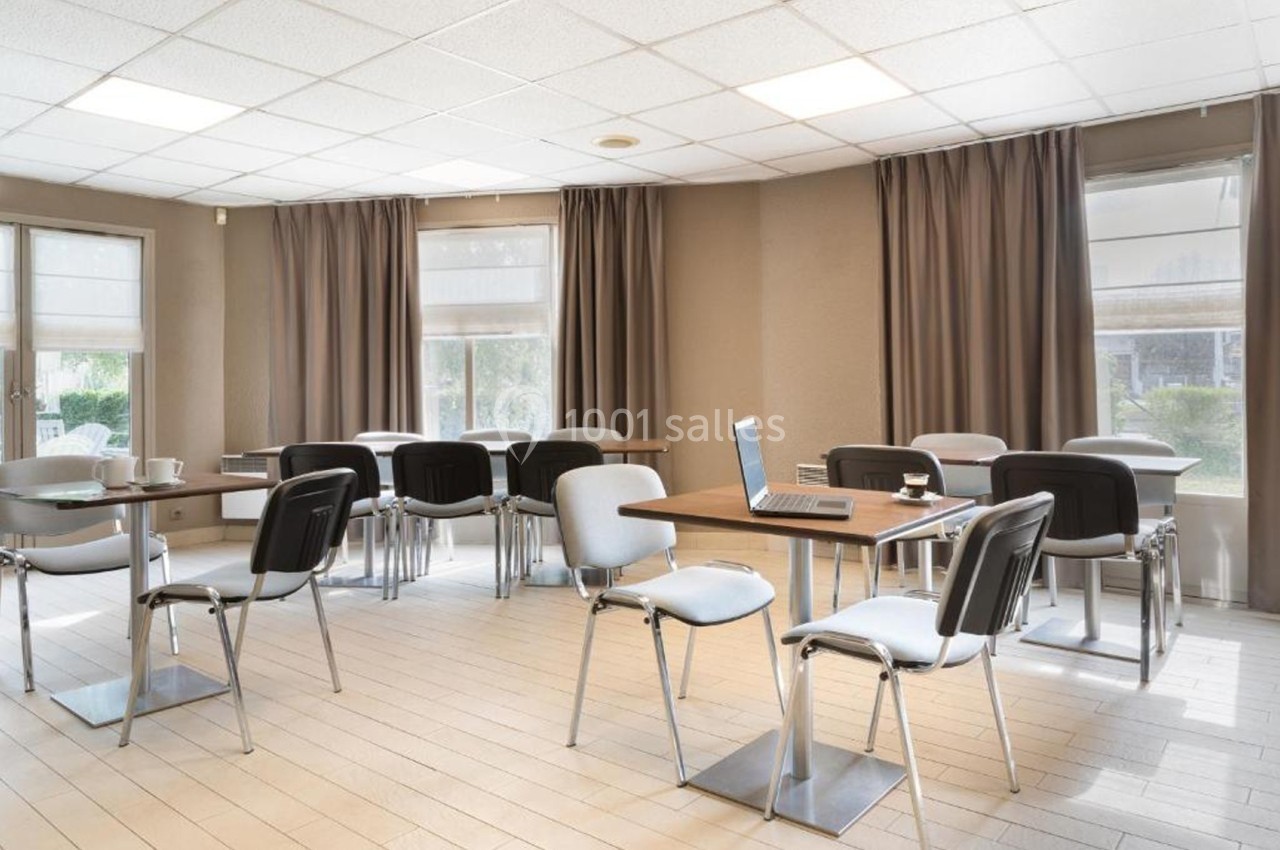 Salle de réunion lumineuse avec des tables, des chaises et un ordinateur portable posé sur une table.