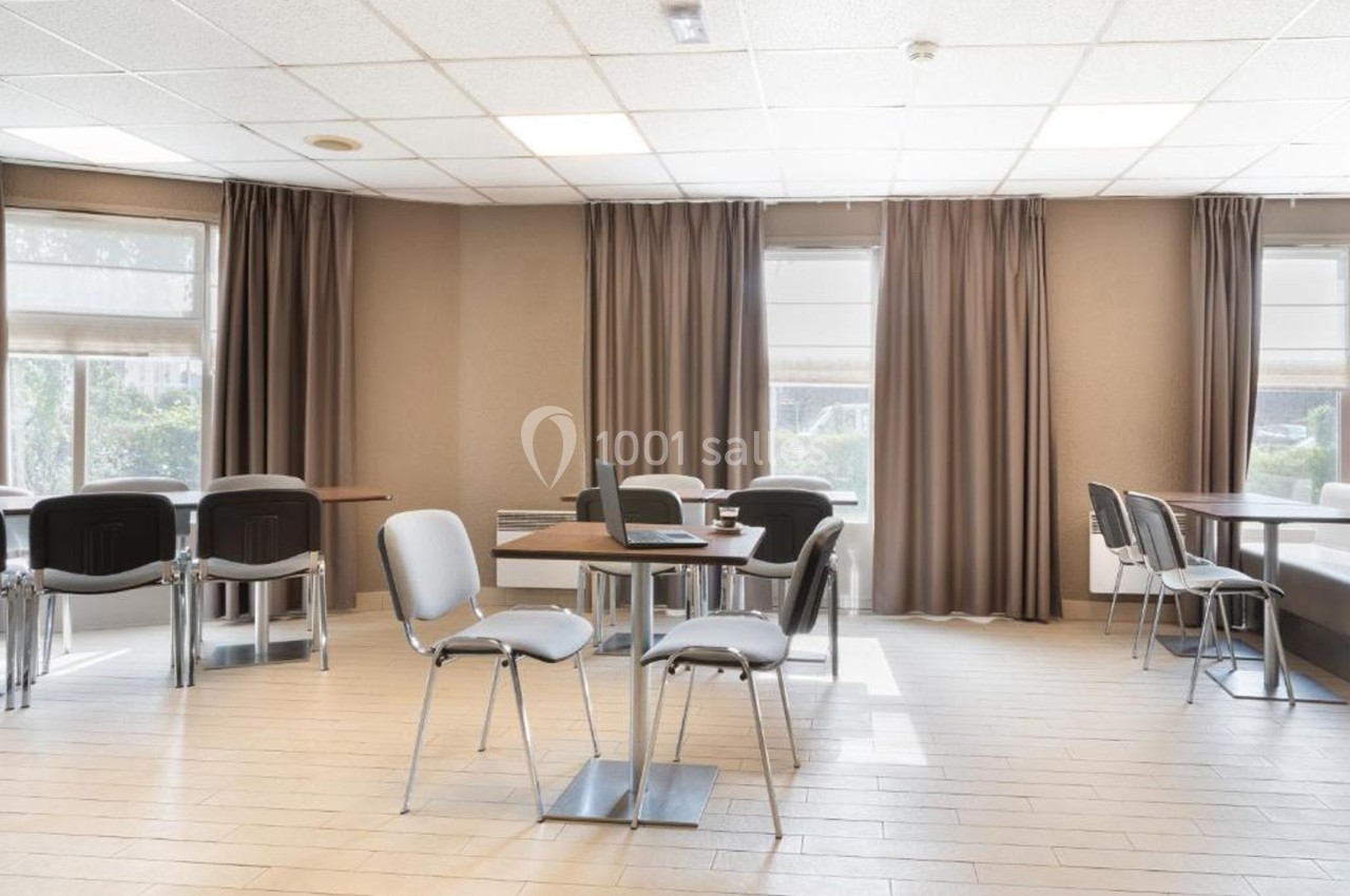 Salle lumineuse avec des tables et des chaises modernes, entourée de grandes fenêtres avec rideaux.
