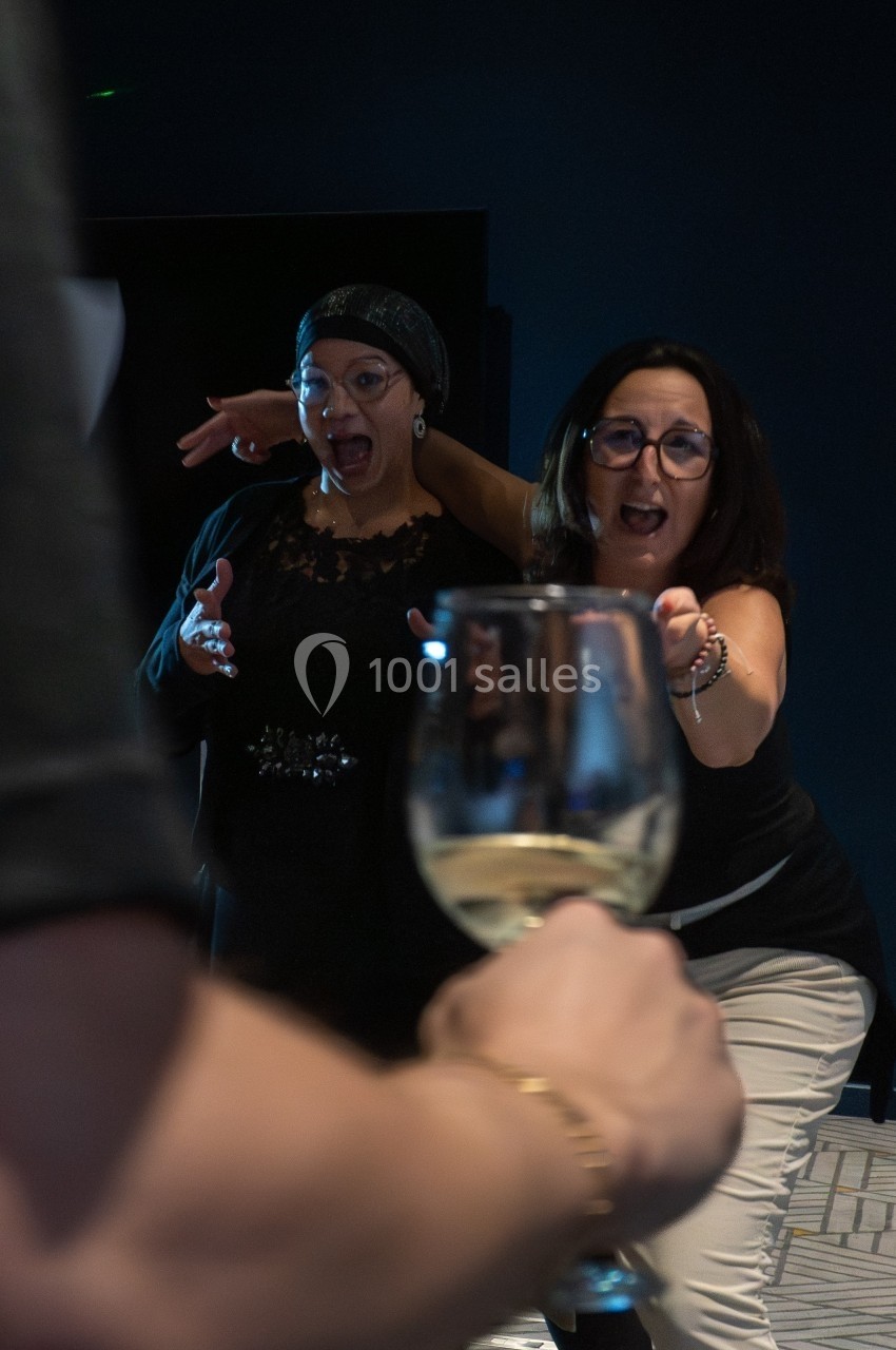 Deux femmes réagissent avec surprise et amusement en direction d'un verre de vin blanc tendu vers elles.