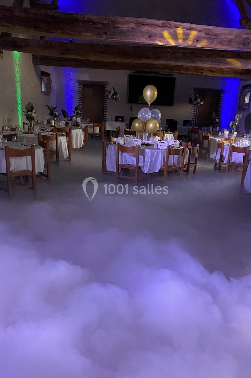 Salle de réception décorée avec des tables dressées, des ballons dorés et un effet de fumée au sol.