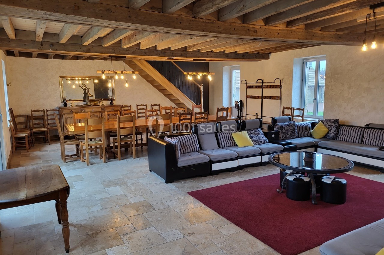 Salle spacieuse avec poutres apparentes, coin salon avec canapés et table basse, et grande table à manger en bois.