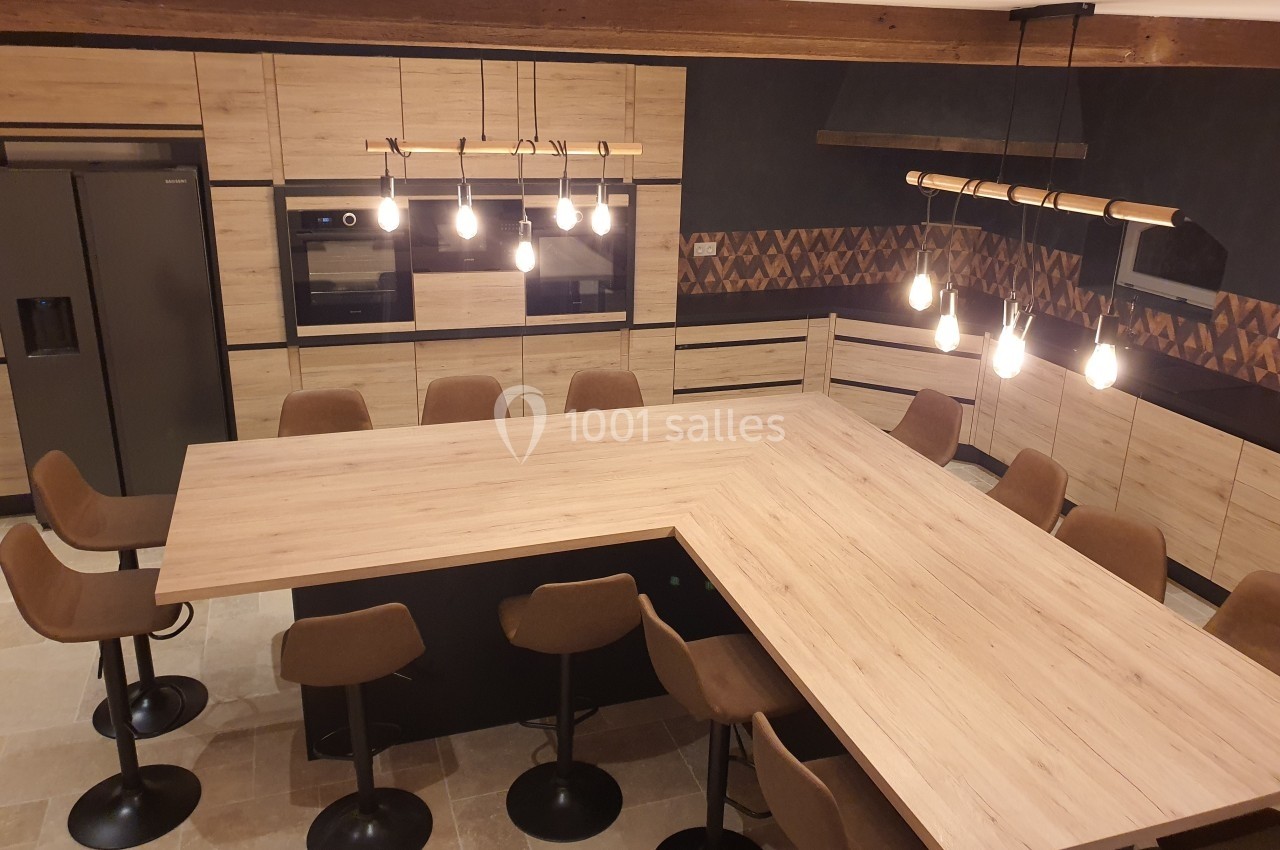 Cuisine moderne avec un grand îlot central en bois, entouré de tabourets, éclairée par des suspensions lumineuses.