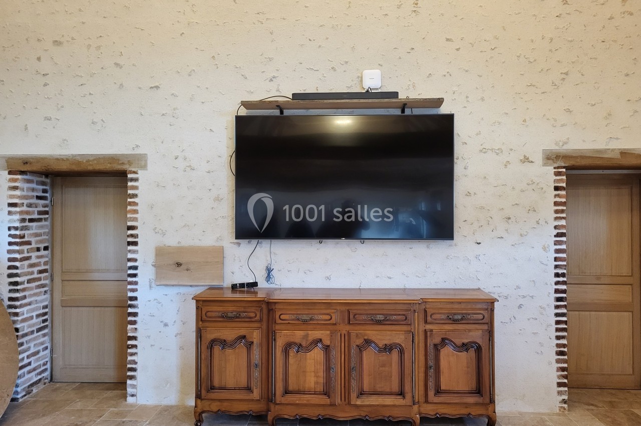 Télévision murale fixée au-dessus d'un buffet en bois sculpté, encadrée par deux portes sur un mur en pierre.