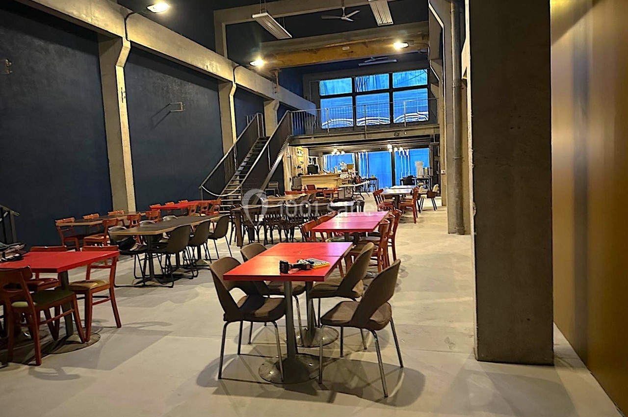 Salle spacieuse avec tables et chaises colorées, éclairage tamisé et escalier menant à une mezzanine.