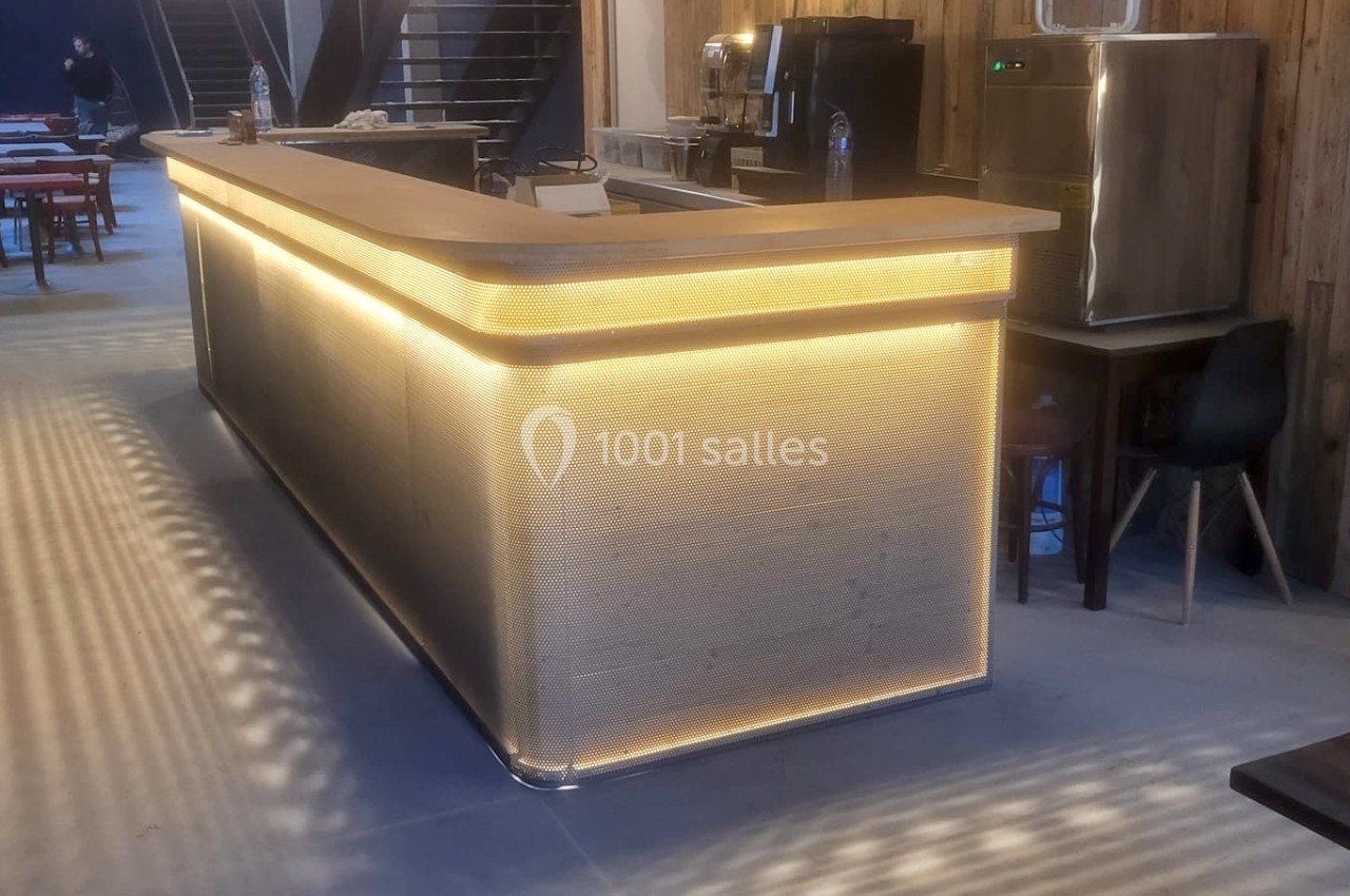 Comptoir de bar moderne éclairé par des LED, avec des tables et chaises en arrière-plan dans un espace intérieur.