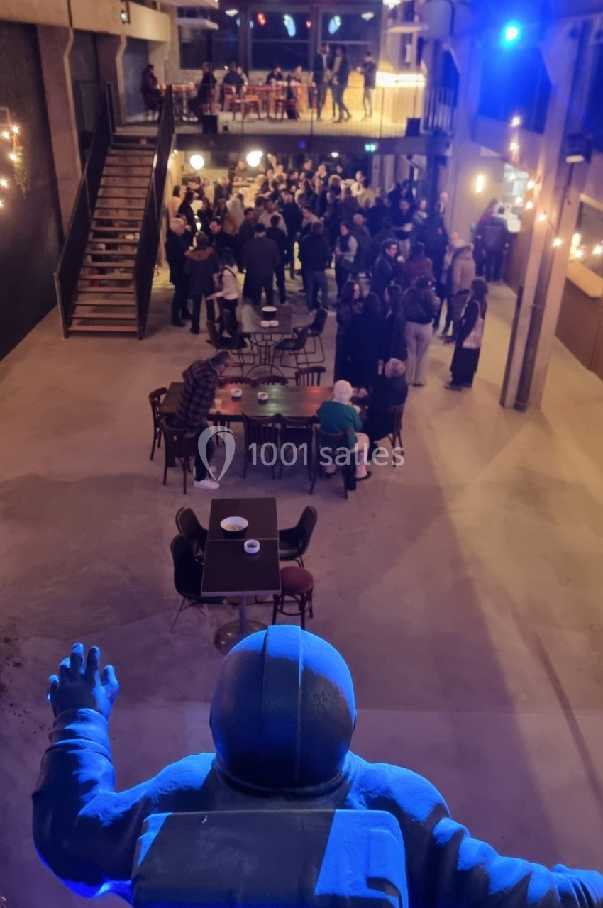 Vue d'une salle animée avec des groupes de personnes debout et assises, observée depuis une statue d'astronaute.