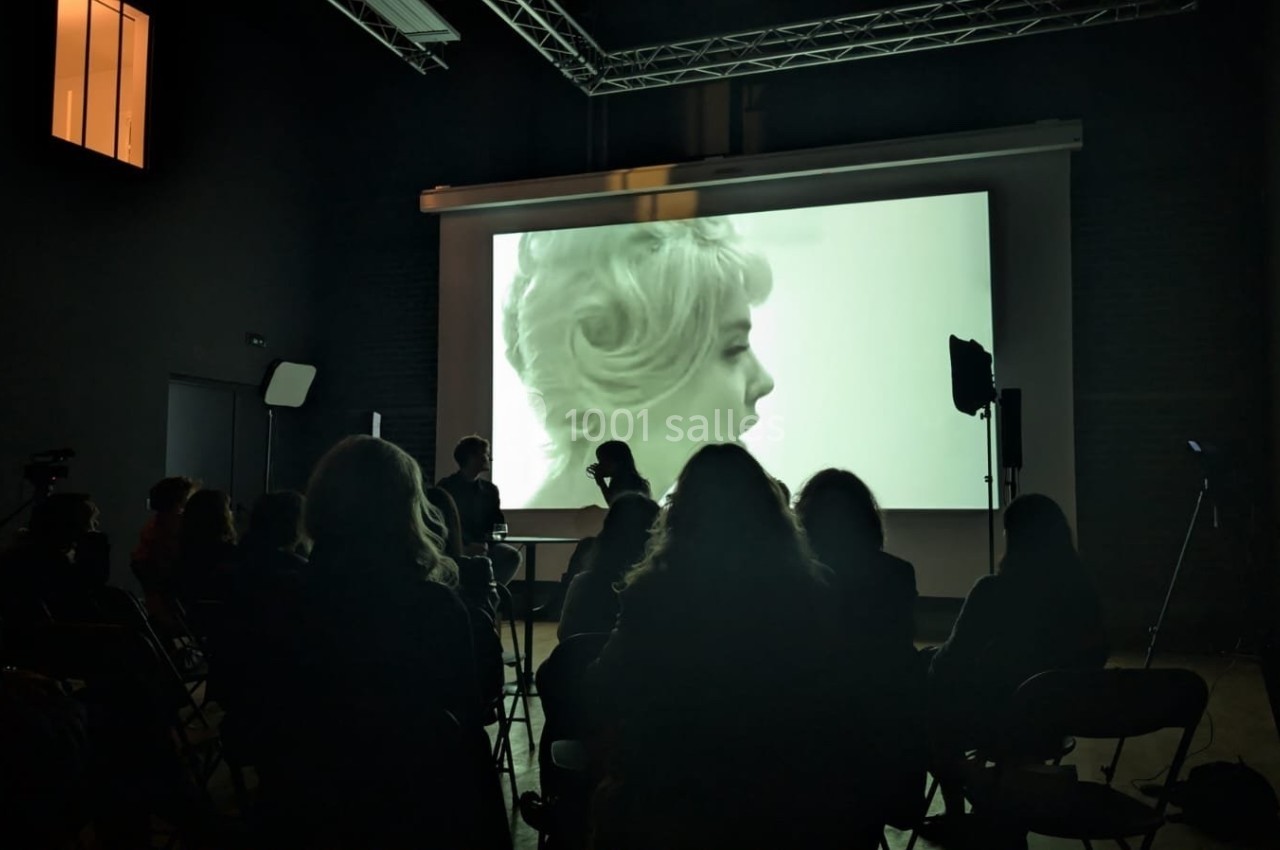Projection d'un film en noir et blanc dans une salle sombre, avec des spectateurs assis devant l'écran.