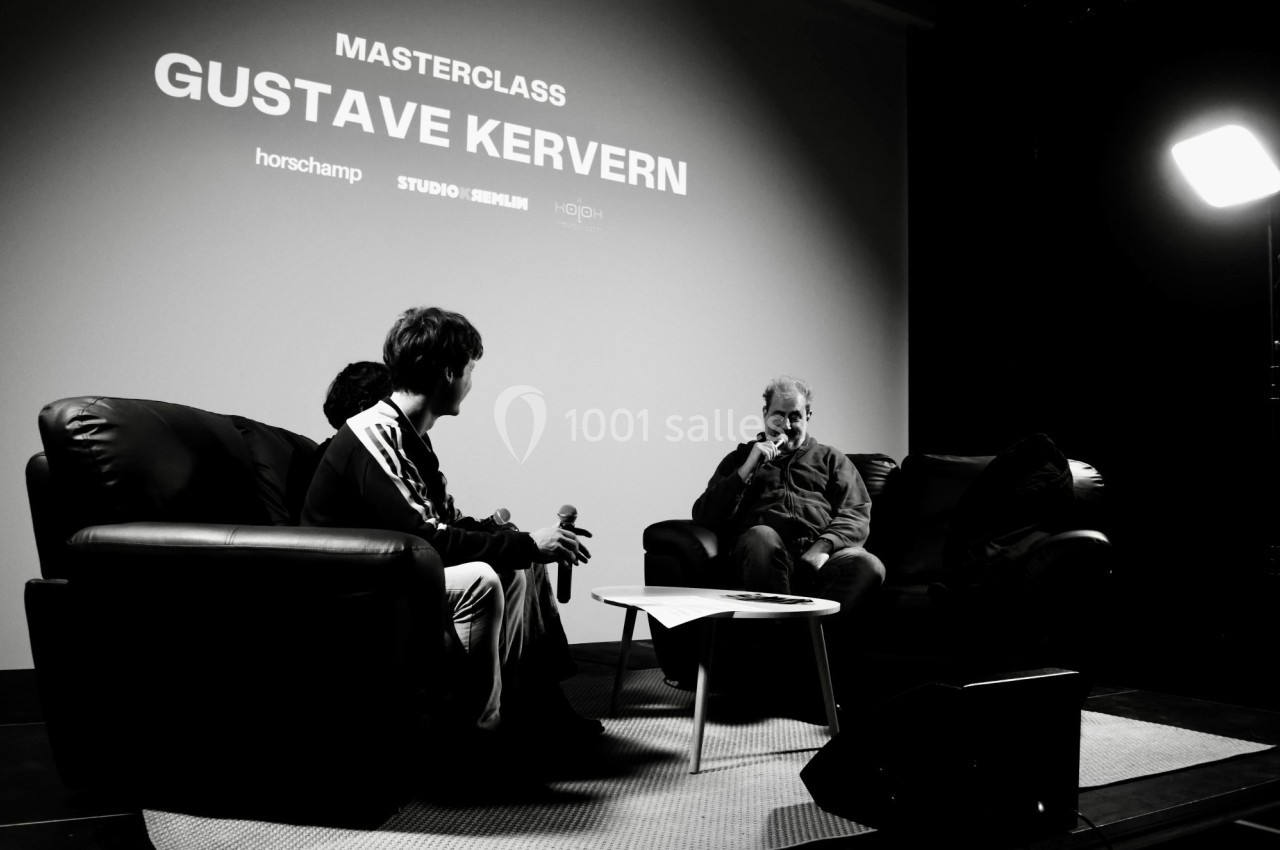 Deux personnes assises sur des fauteuils discutent sur scène lors d'une masterclass, avec un écran en arrière-plan.