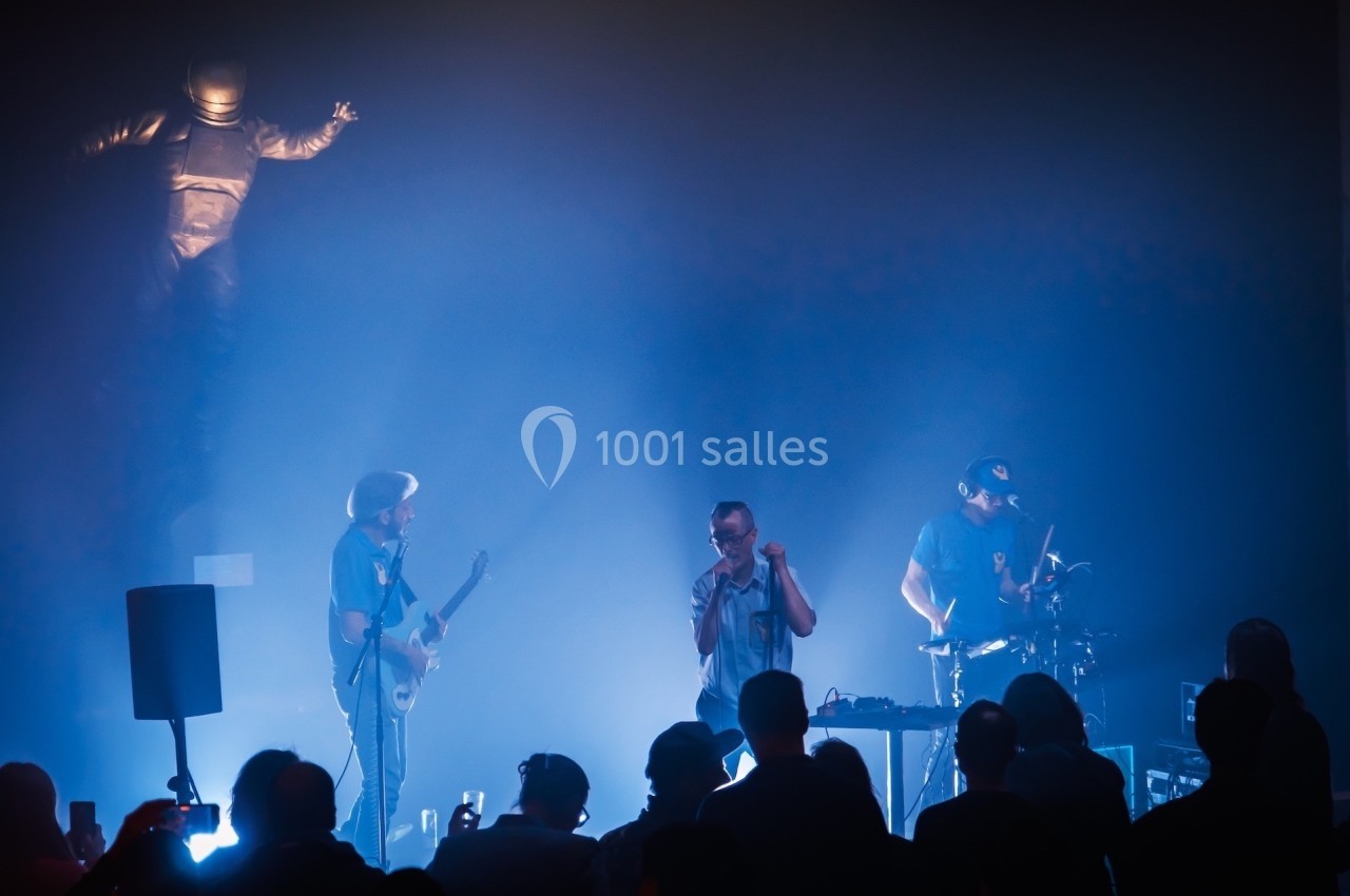 Un groupe de musiciens joue sur scène dans une ambiance lumineuse bleutée, devant un public attentif.