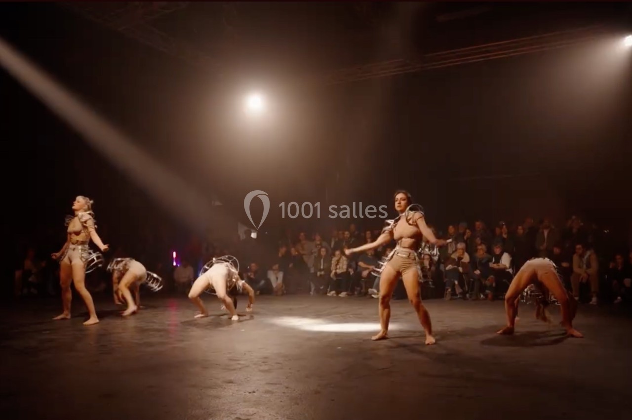 Des danseurs en tenue artistique exécutent une chorégraphie sur une scène éclairée, devant un public.