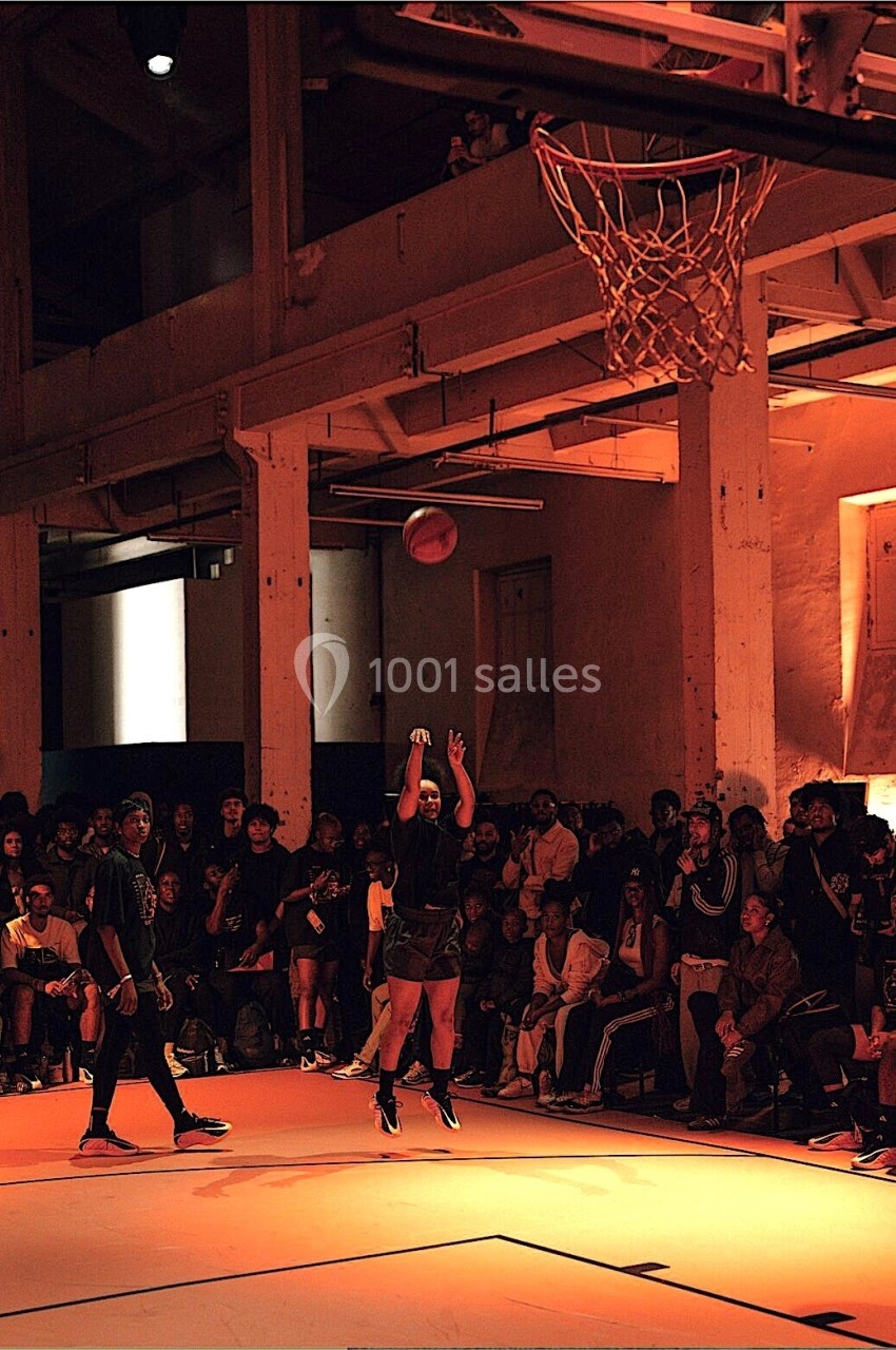 Une joueuse de basketball tire un panier sous les projecteurs, entourée d'un public dans un gymnase.