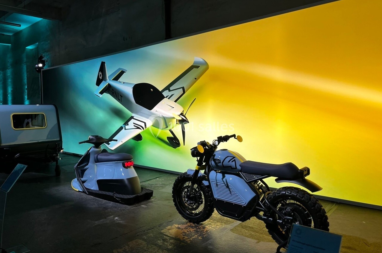 Deux motos électriques exposées devant un mur lumineux avec une illustration d'avion futuriste.