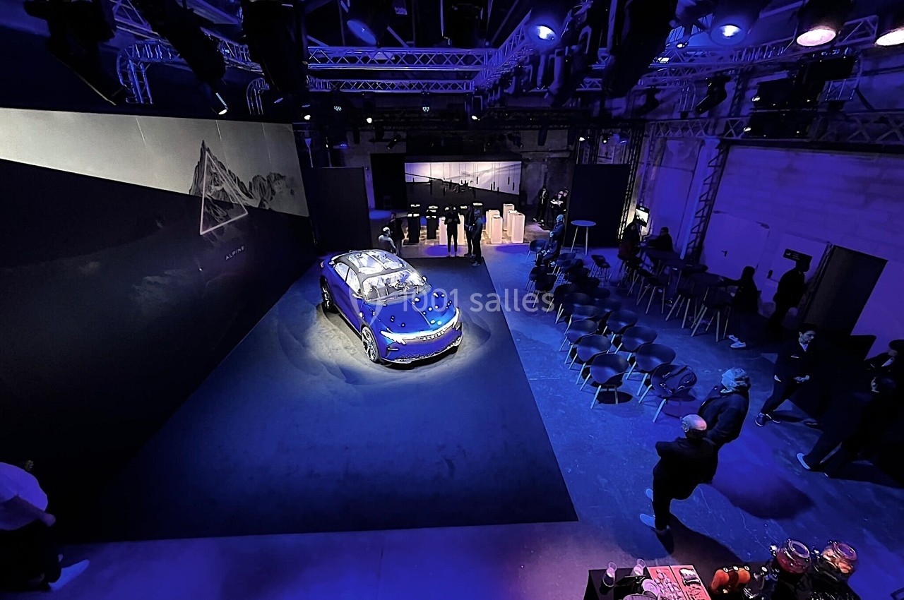 Voiture électrique exposée dans un espace sombre éclairé par des lumières violettes, avec des sièges et un écran en arrière…