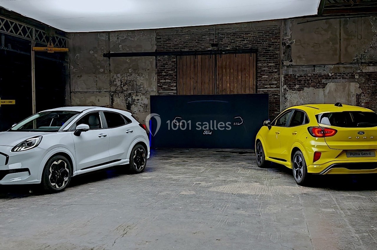 Deux voitures compactes, une blanche et une jaune, stationnées dans un entrepôt au style industriel.