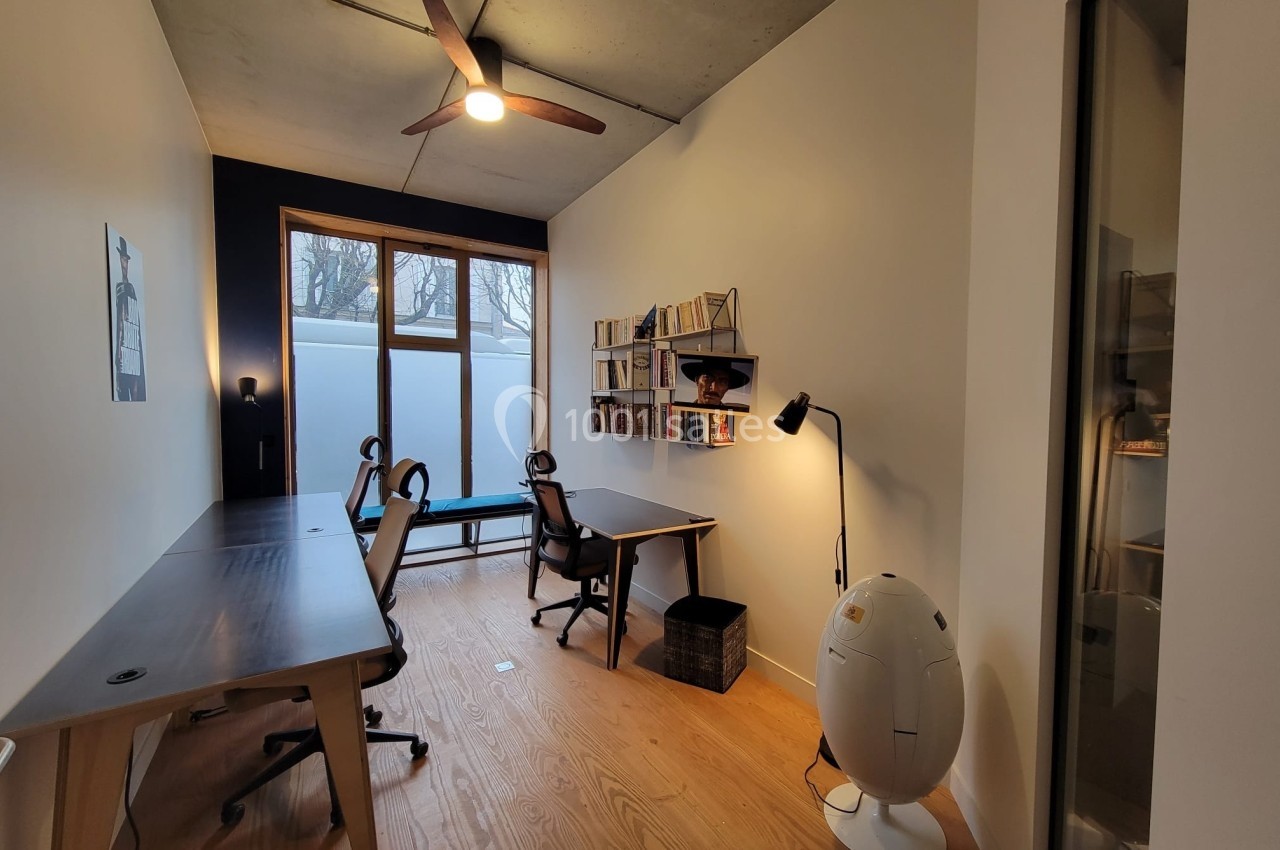 Bureau moderne avec deux postes de travail, étagères murales, lampe sur pied et grande fenêtre laissant entrer la lumière…