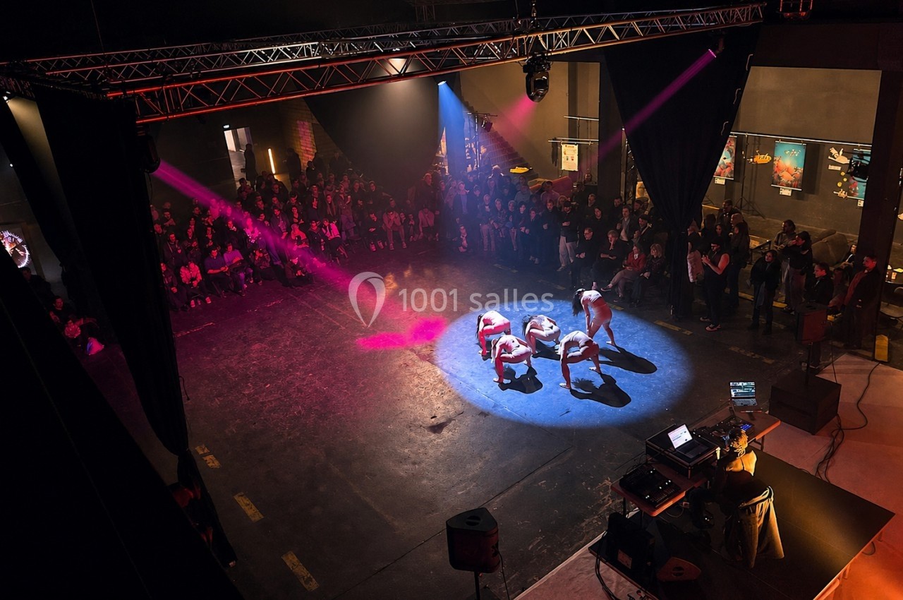 Quatre danseurs exécutent une performance au centre d'une scène éclairée, entourés d'un public debout.